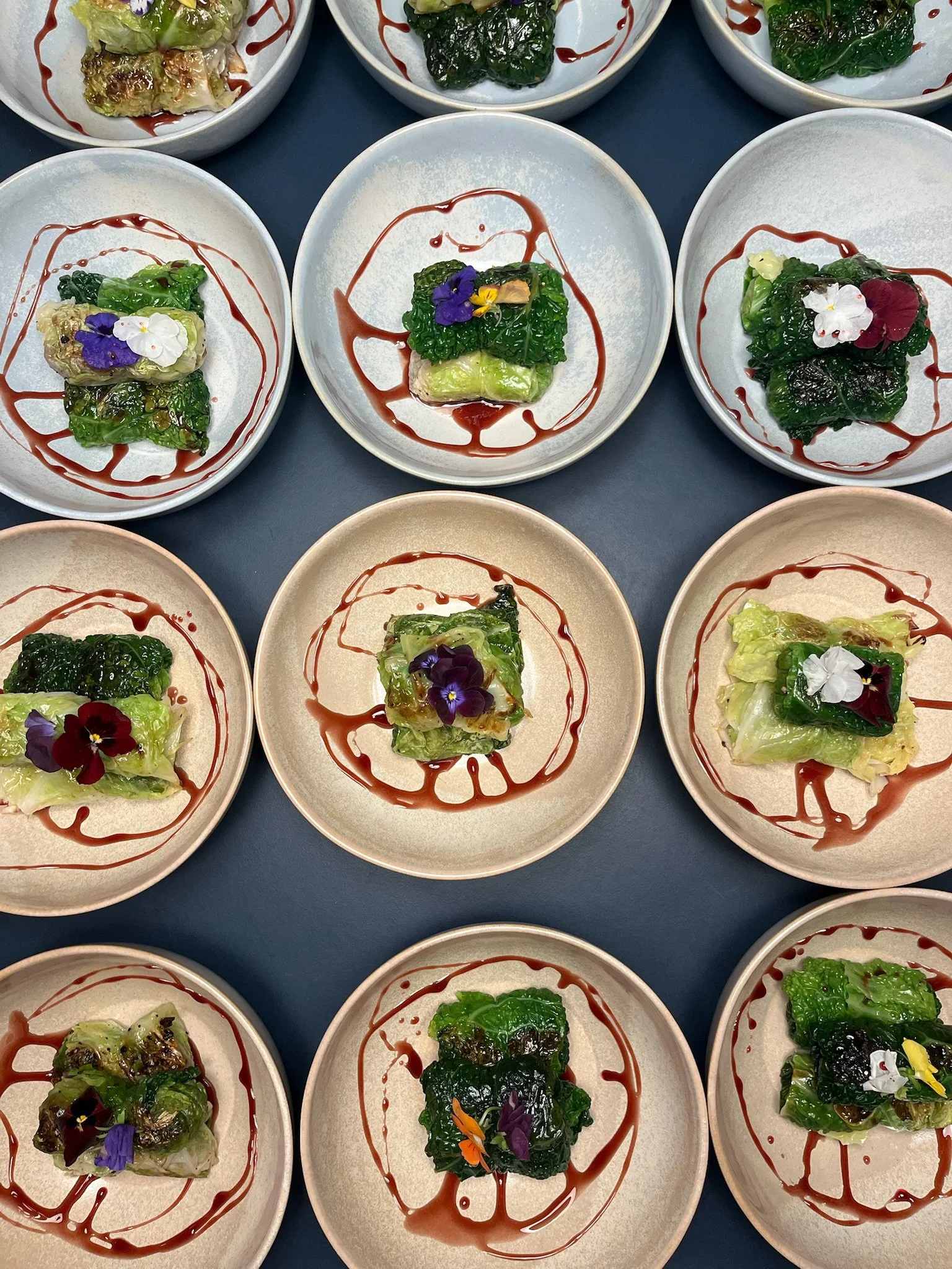 Små tallerkener med indpakkede salater toppet med spiselige blomster og dryppet med sauce.