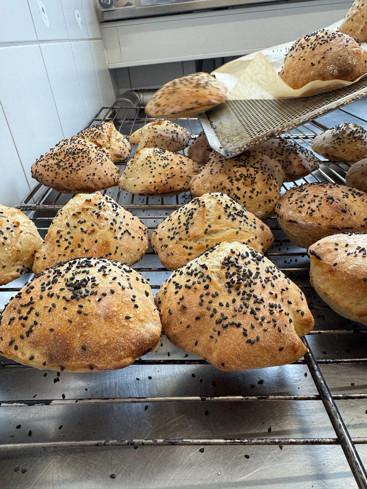 Friskbagte surdejsboller står til afkøling i et industrikøkken.