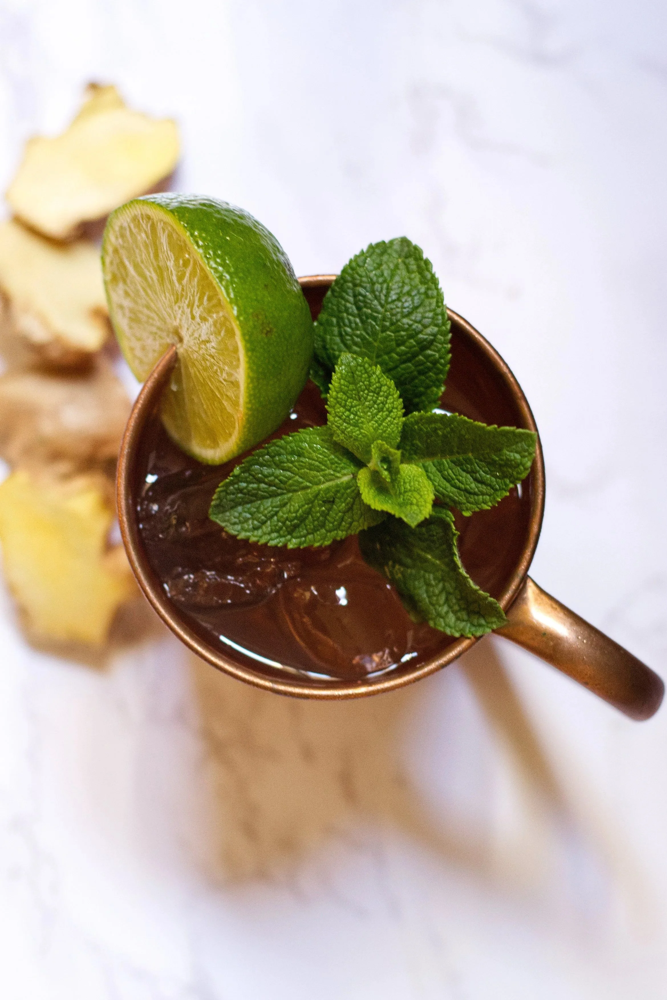 Close-up of Wolfshmidt Kümmels recommended cocktail "The Scandi Mule" in a copper goblet filled with ice, garnished with a sprig of fresh mint and a wedge of lime.
