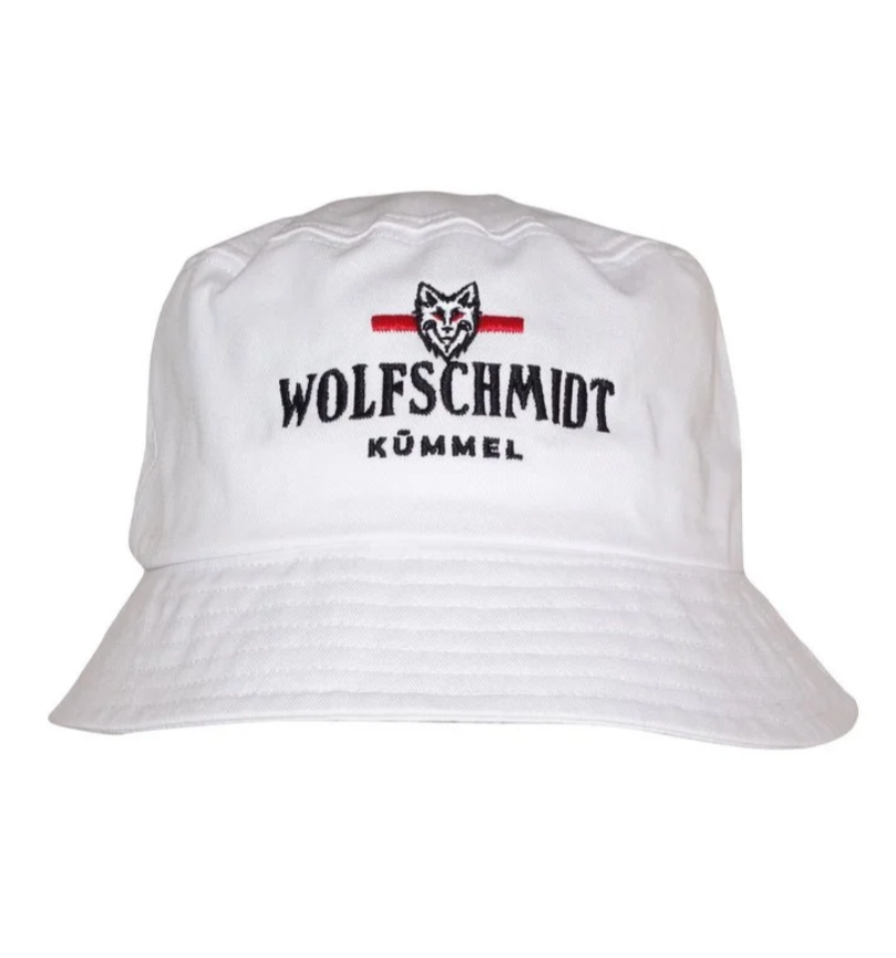 White bucket hat with embroidered logo and text reading "WOLFSCHMIDT KÜMMEL," featuring a wolf's head graphic with a red line above it.