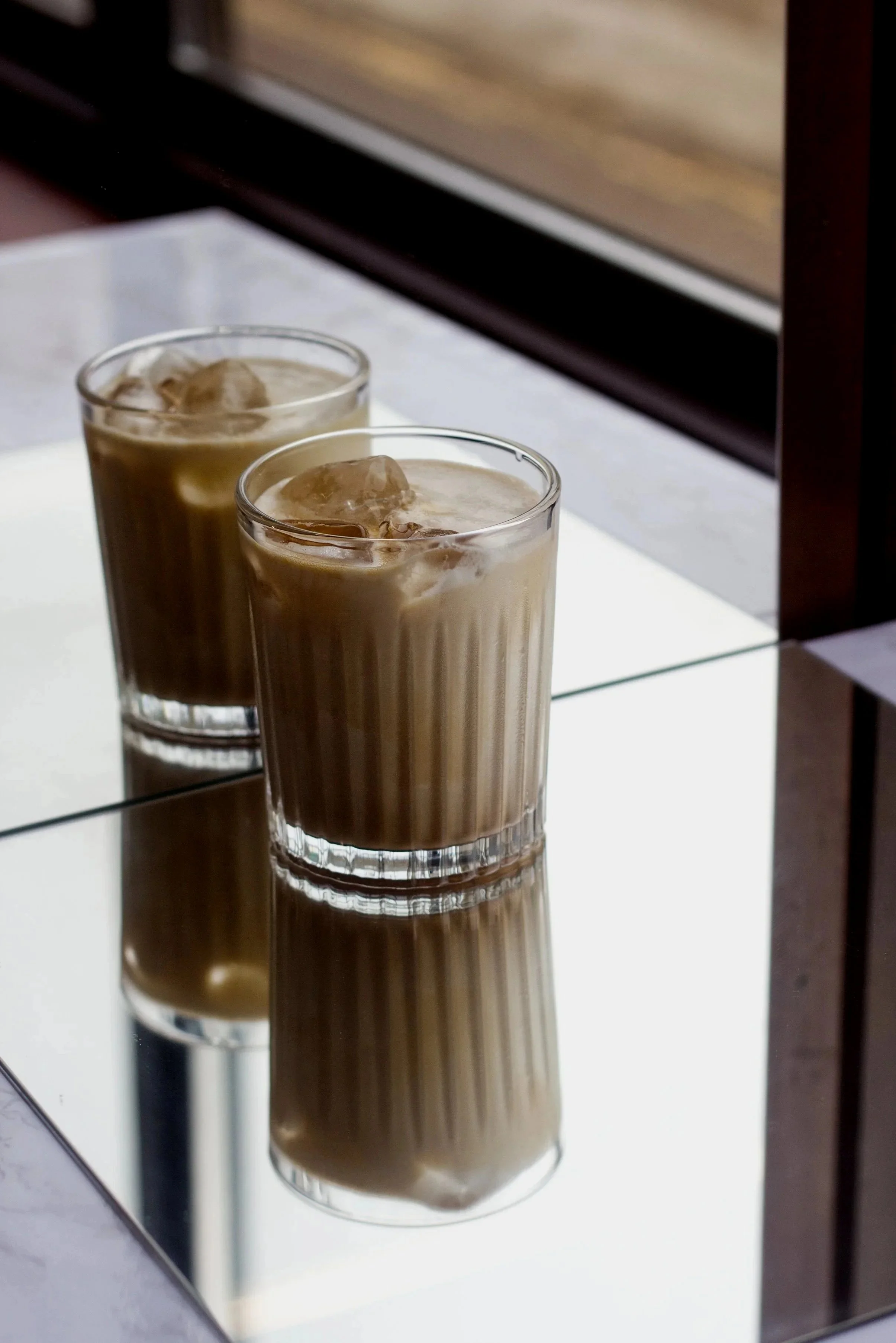 Wolfschmidt Kümmel's recomended "after hours" cocktail showing a cut glass tumbler filled with iced coffee, set on a mirrored surface with a wooden drawer in the background.