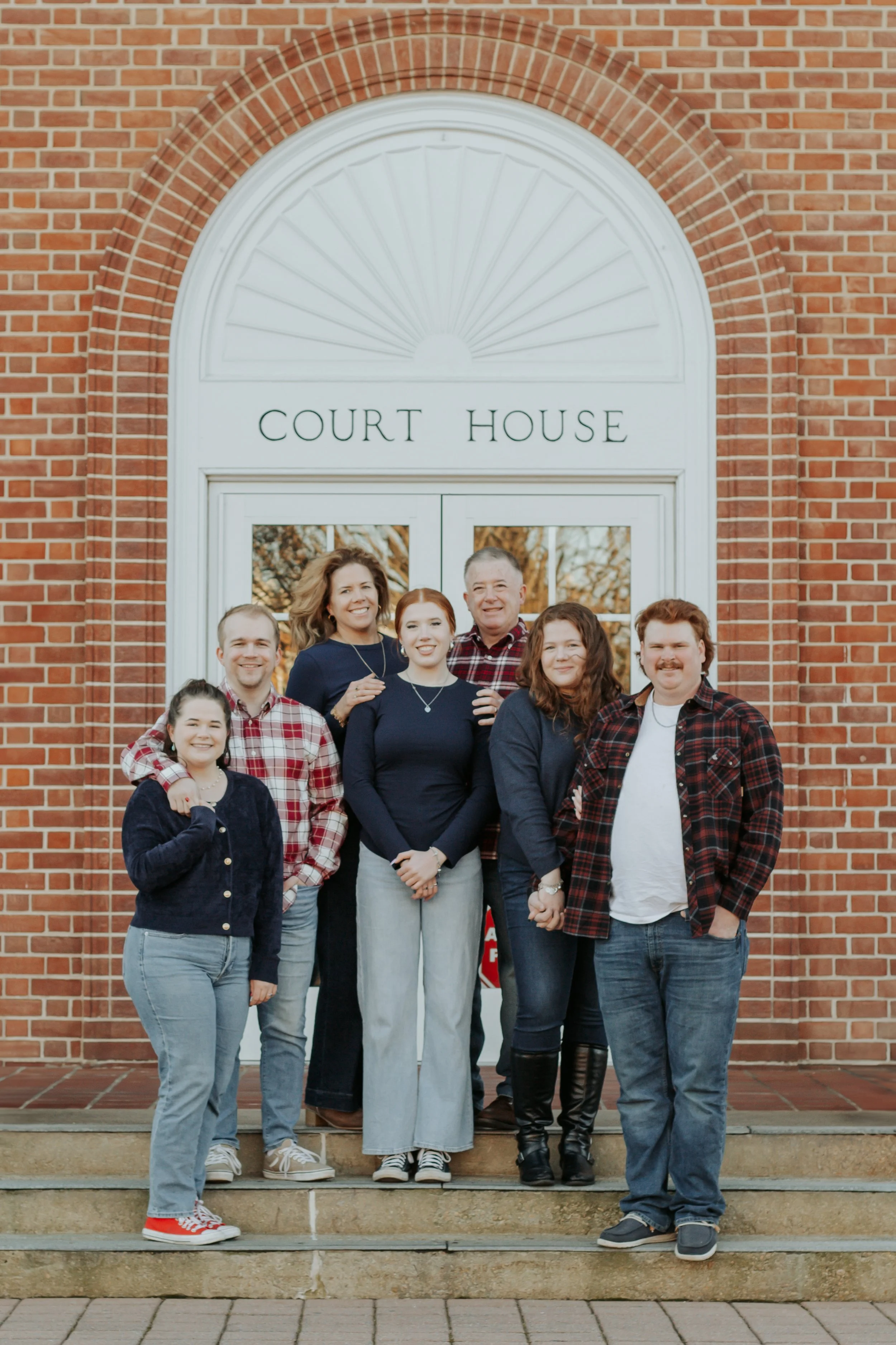 A family standing on the steps in front of the court house with a brick facade, posing for a photo.