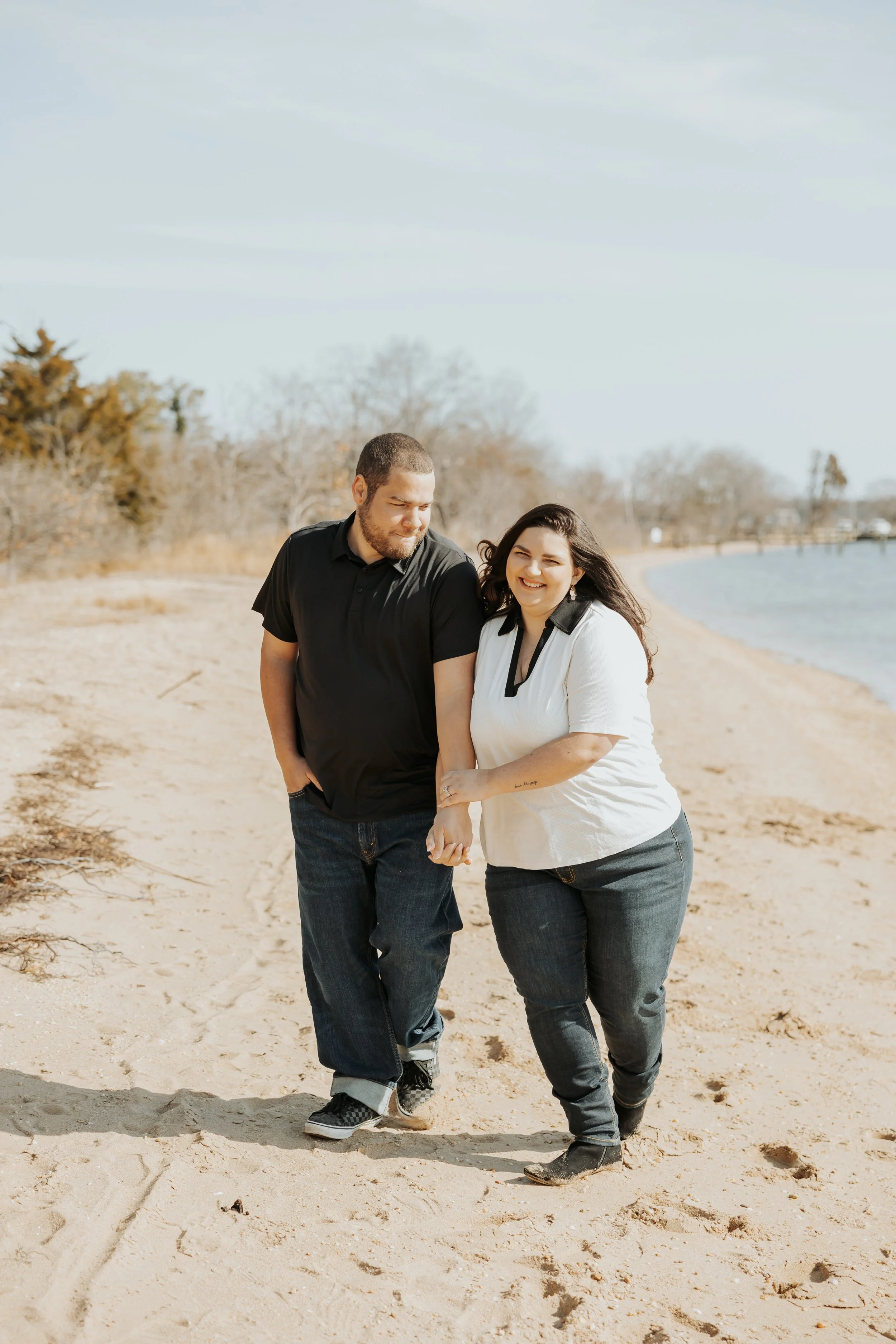 A happy couple walking on a sandy beach, holding hands and smiling.