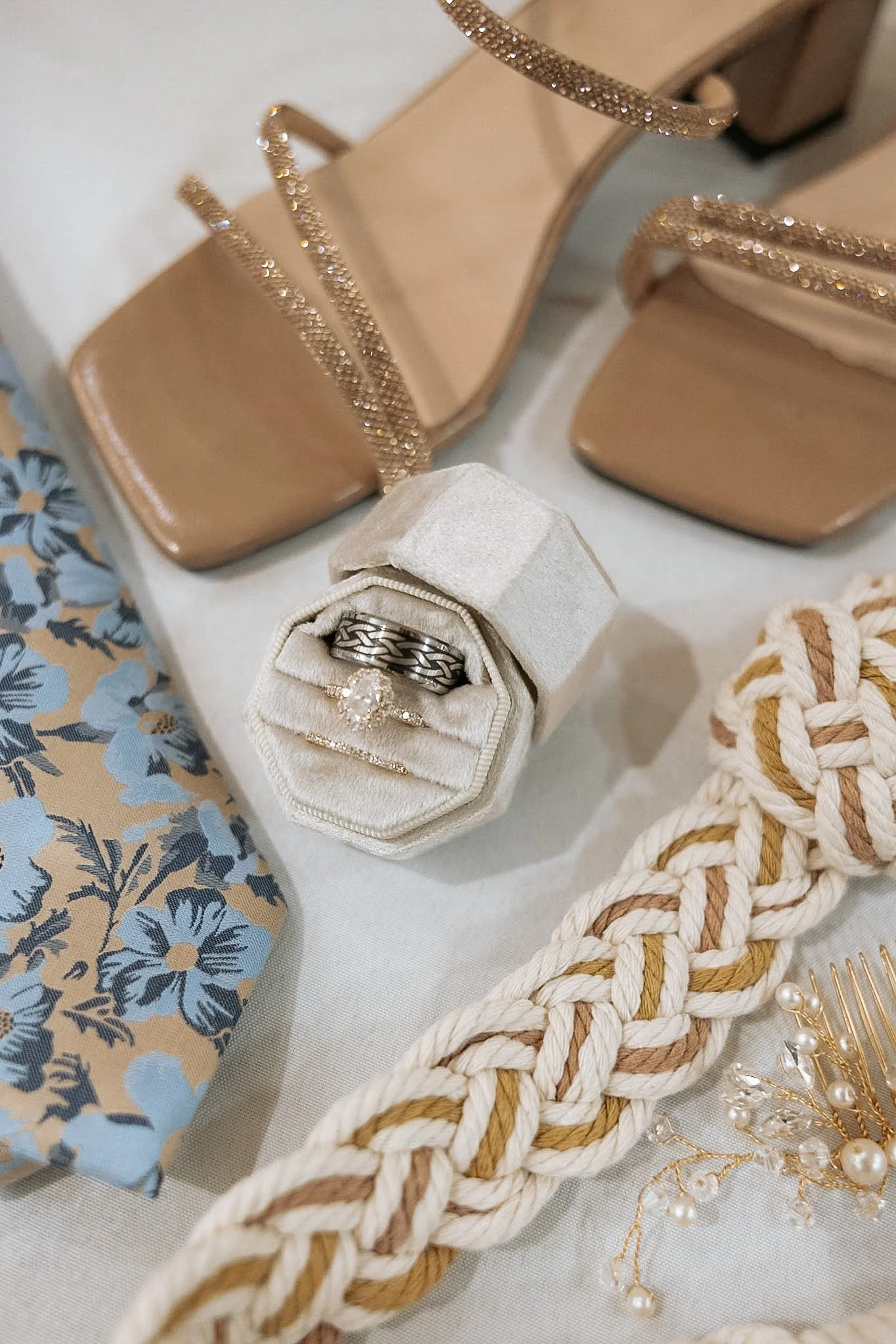Display of jewelry including rings, a bracelet, and accessories on a decorative table with handbags, a braided rope, and floral fabric.