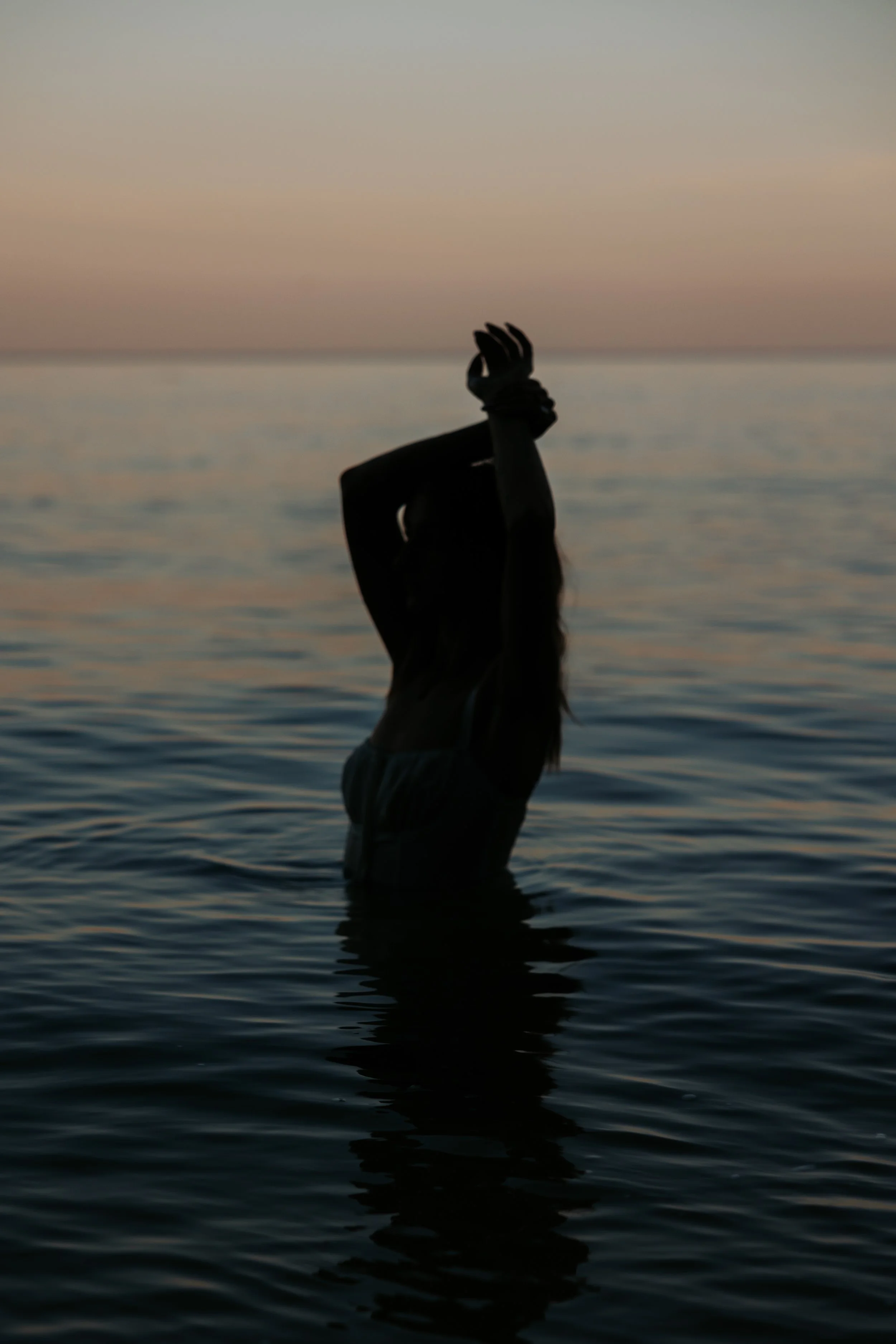 Silhouette of a woman standing in water during sunset or sunrise with sky in pastel pink and blue hues in the background.