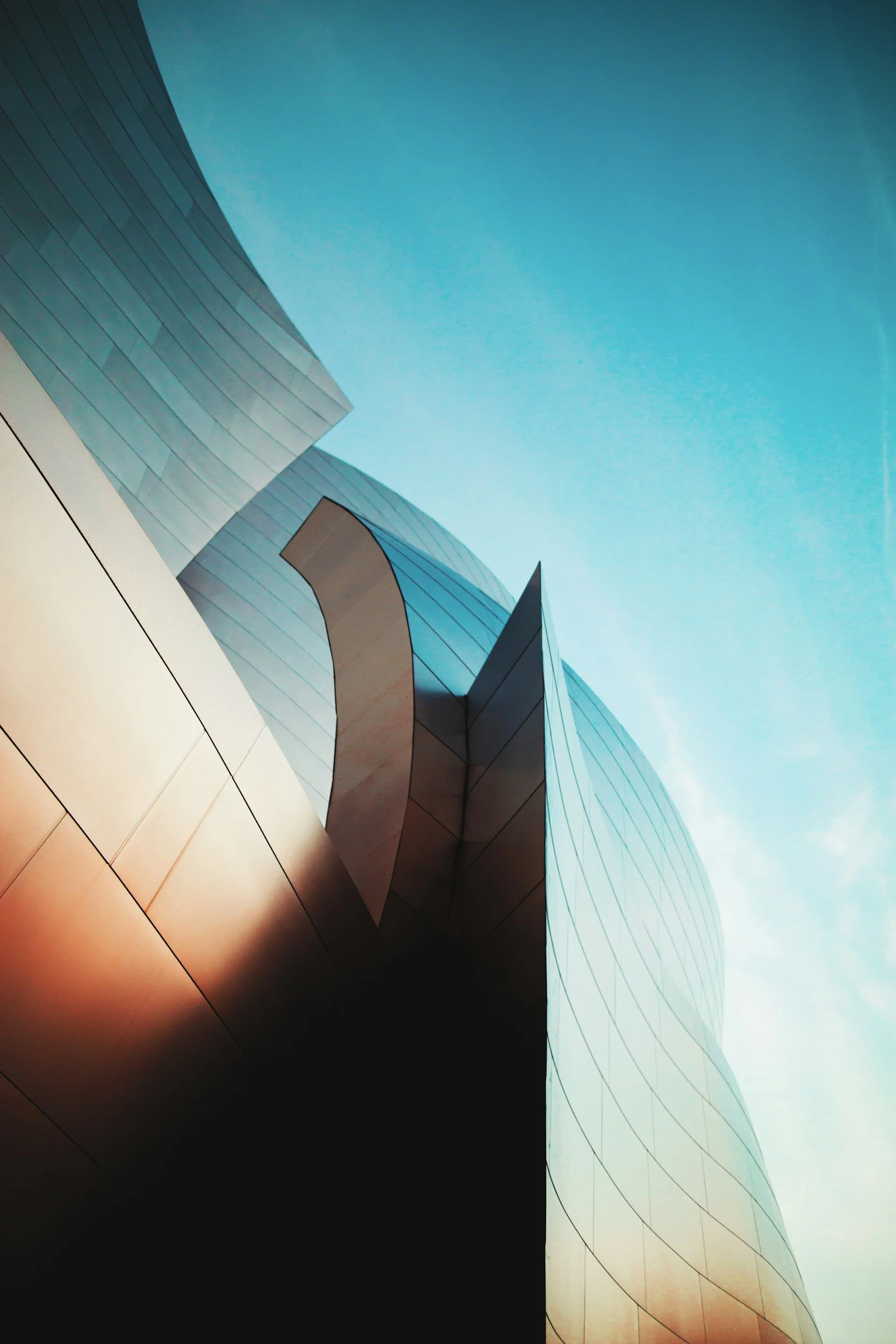 Close-up of modern glass and metal building with curved architectural features against a blue sky.