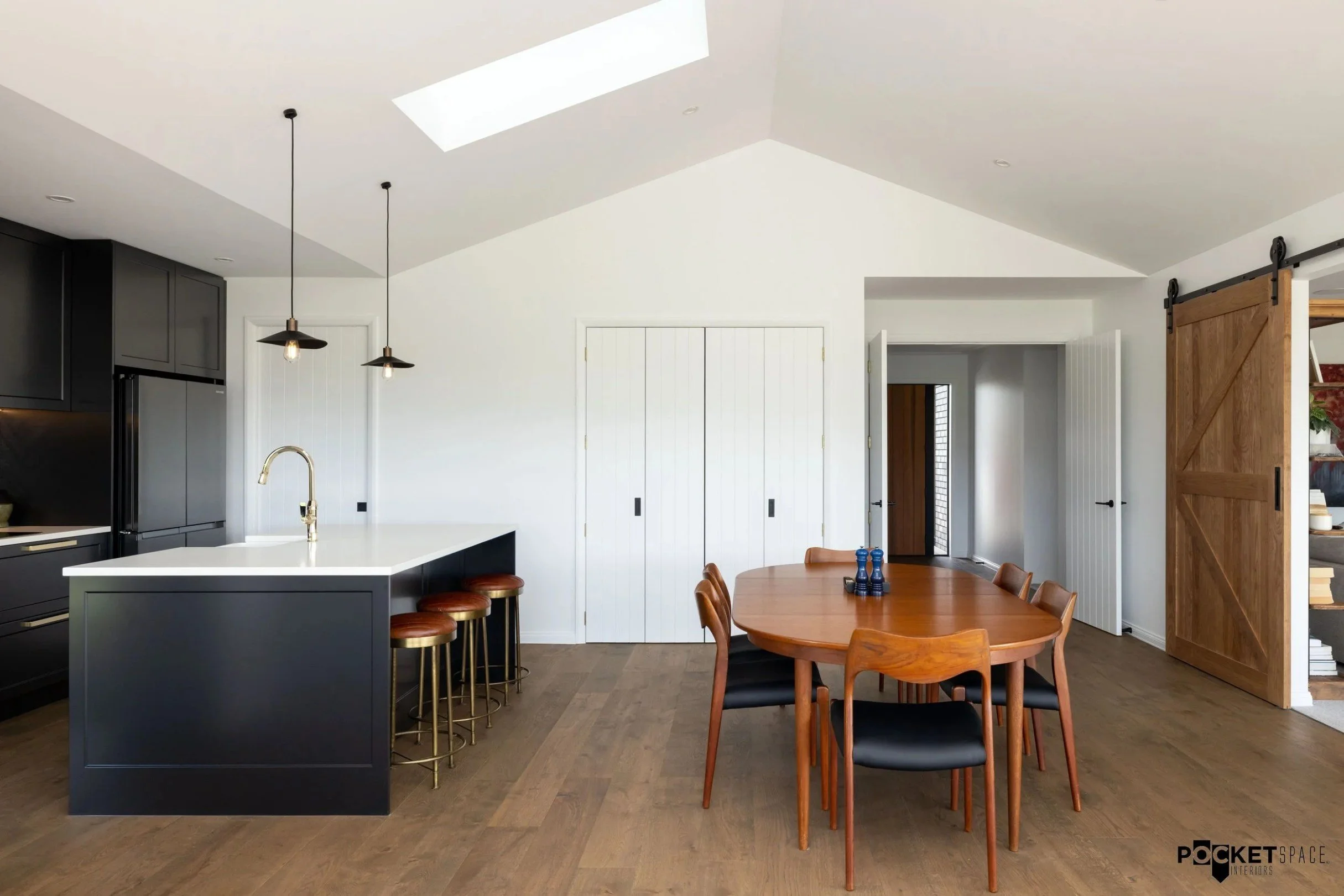 Modern kitchen and dining area with black cabinets, white countertops, wooden dining table, and sliding barn door.