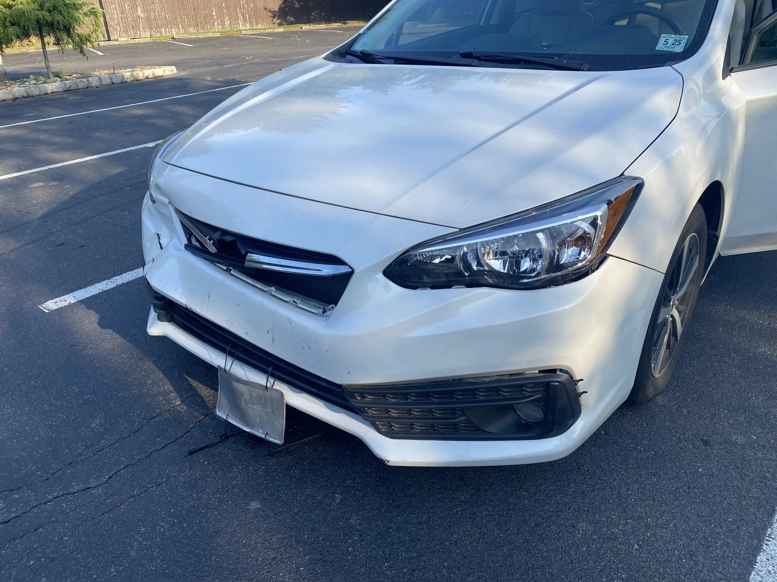 White sedan with front-end damage parked in an empty parking lot.