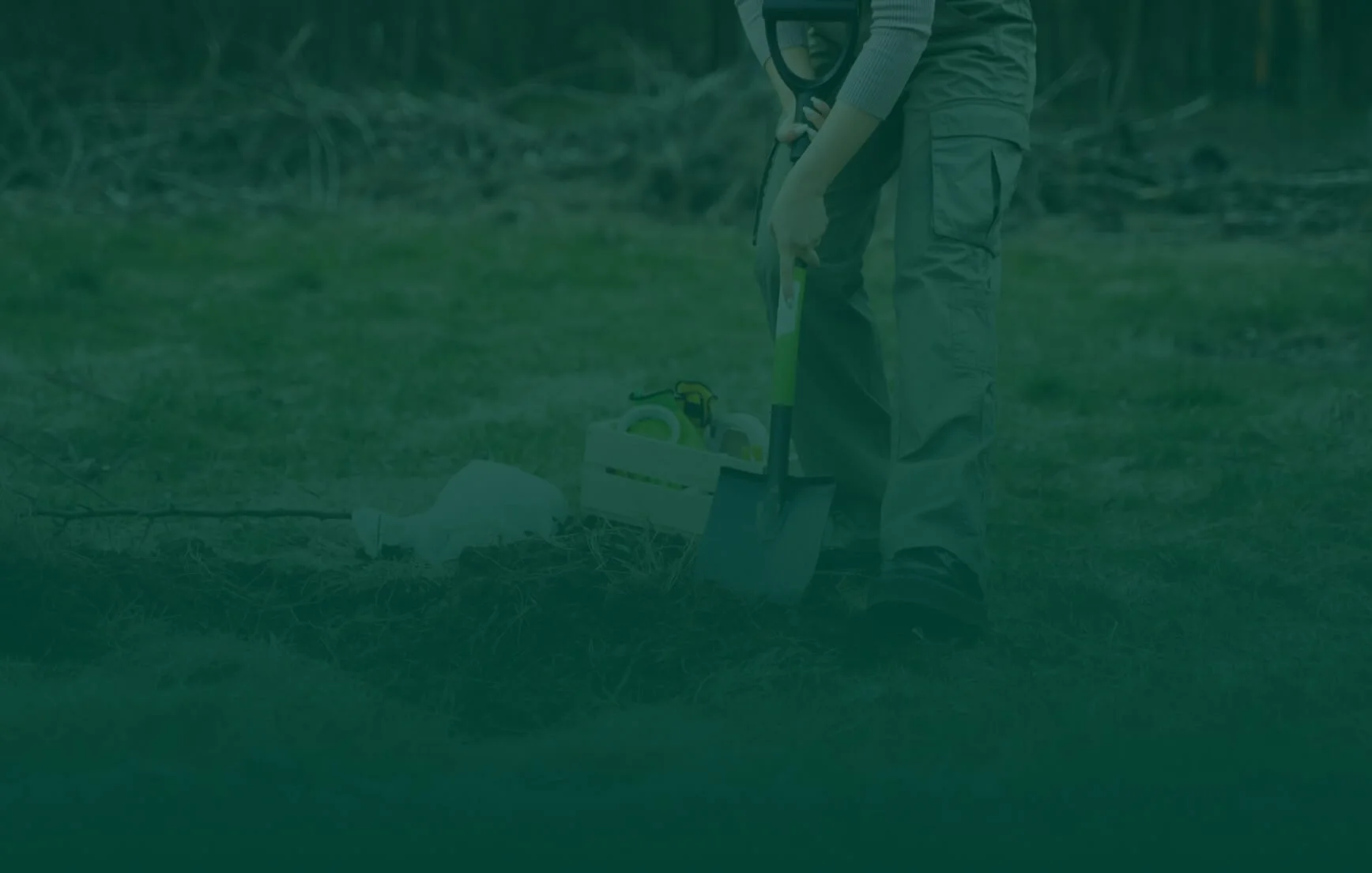 Person wearing work boots and work pants using a chainsaw to cut a tree branch in a grassy outdoor area.