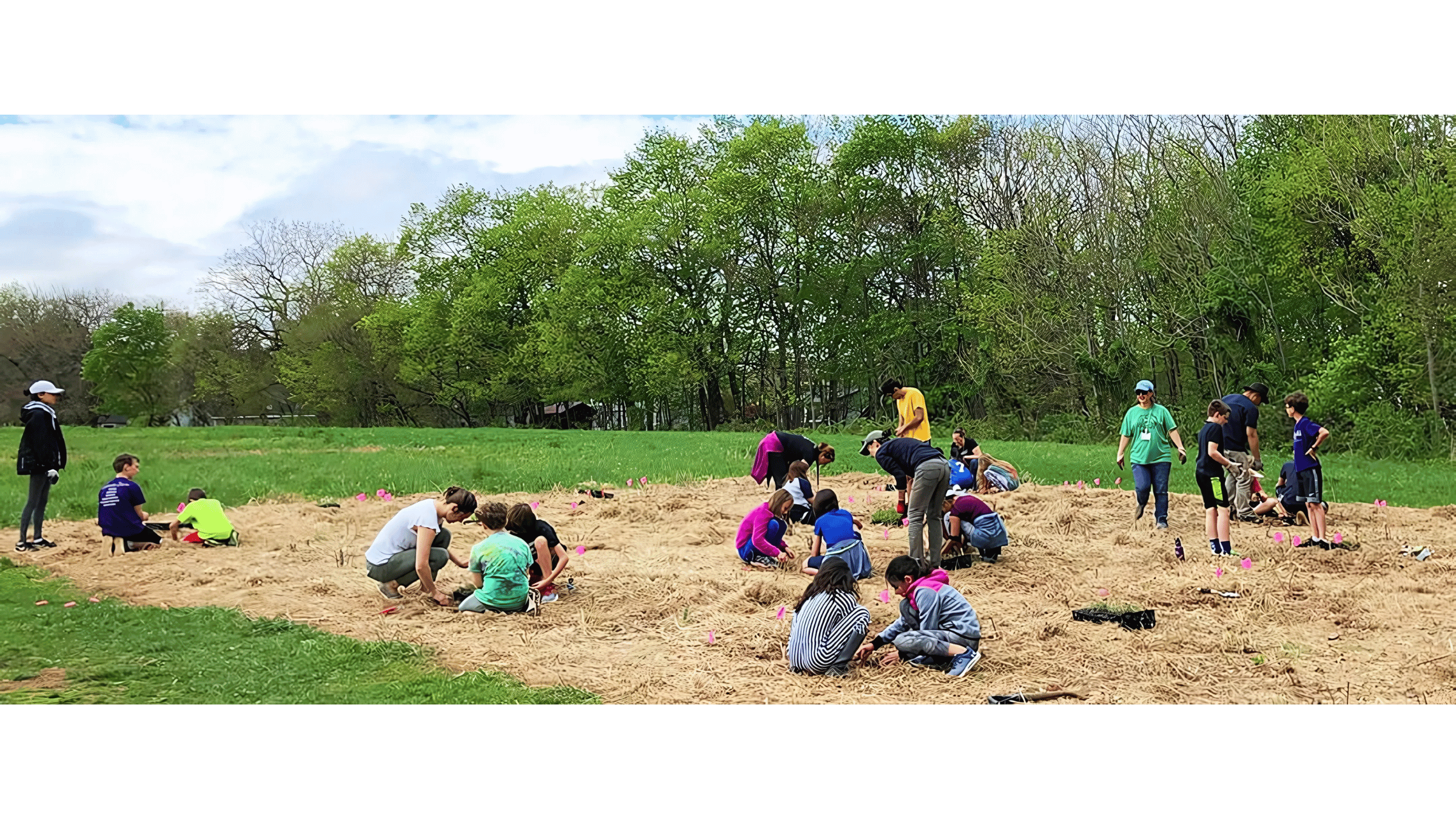 Children and adults planting flowers in a community garden, with green trees and a cloudy sky in the background.