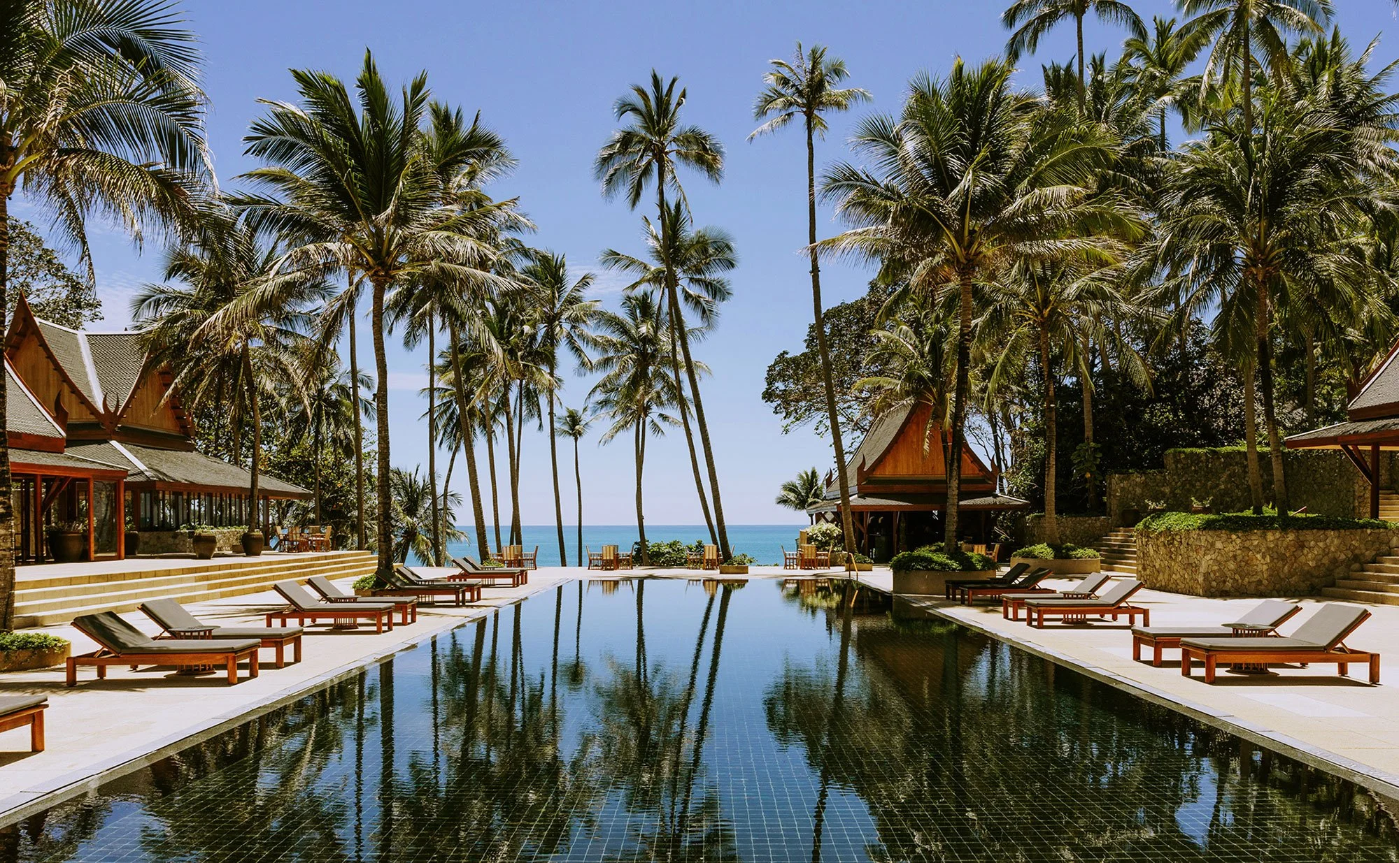 Amanpuri resort in Phuket with palm trees, traditional Thai architecture, sun loungers, and an infinity pool overlooking the sea.
