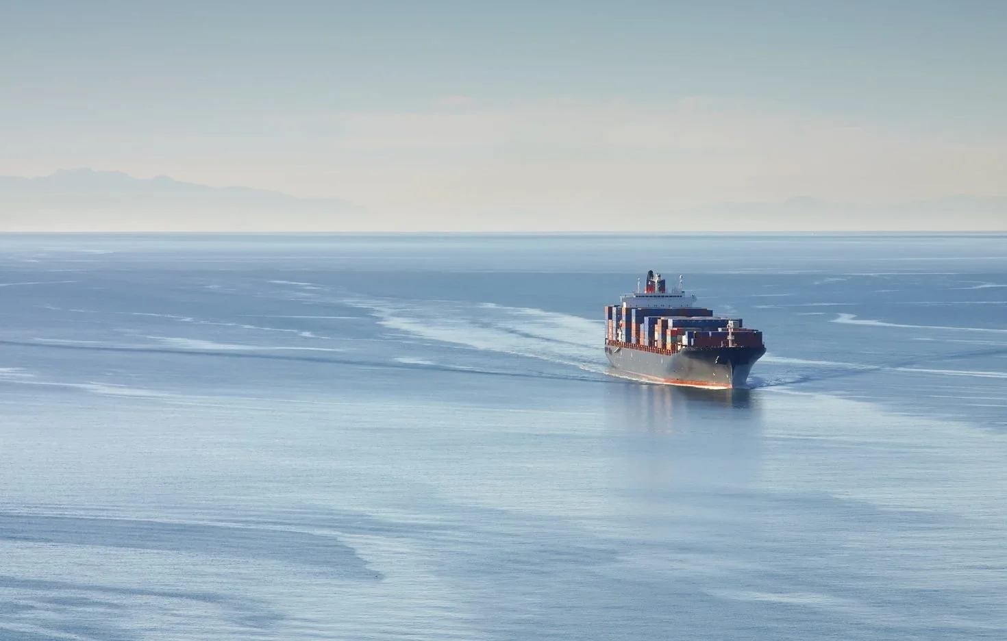 A large cargo ship cuts across calm open waters, symbolizing global trade and international logistics.