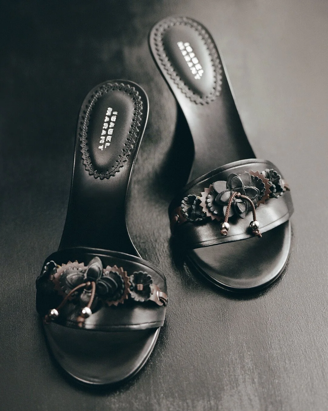 Isabel Marant black leather sandals with handcrafted floral detailing reflecting the brand’s Parisian bohemian aesthetic