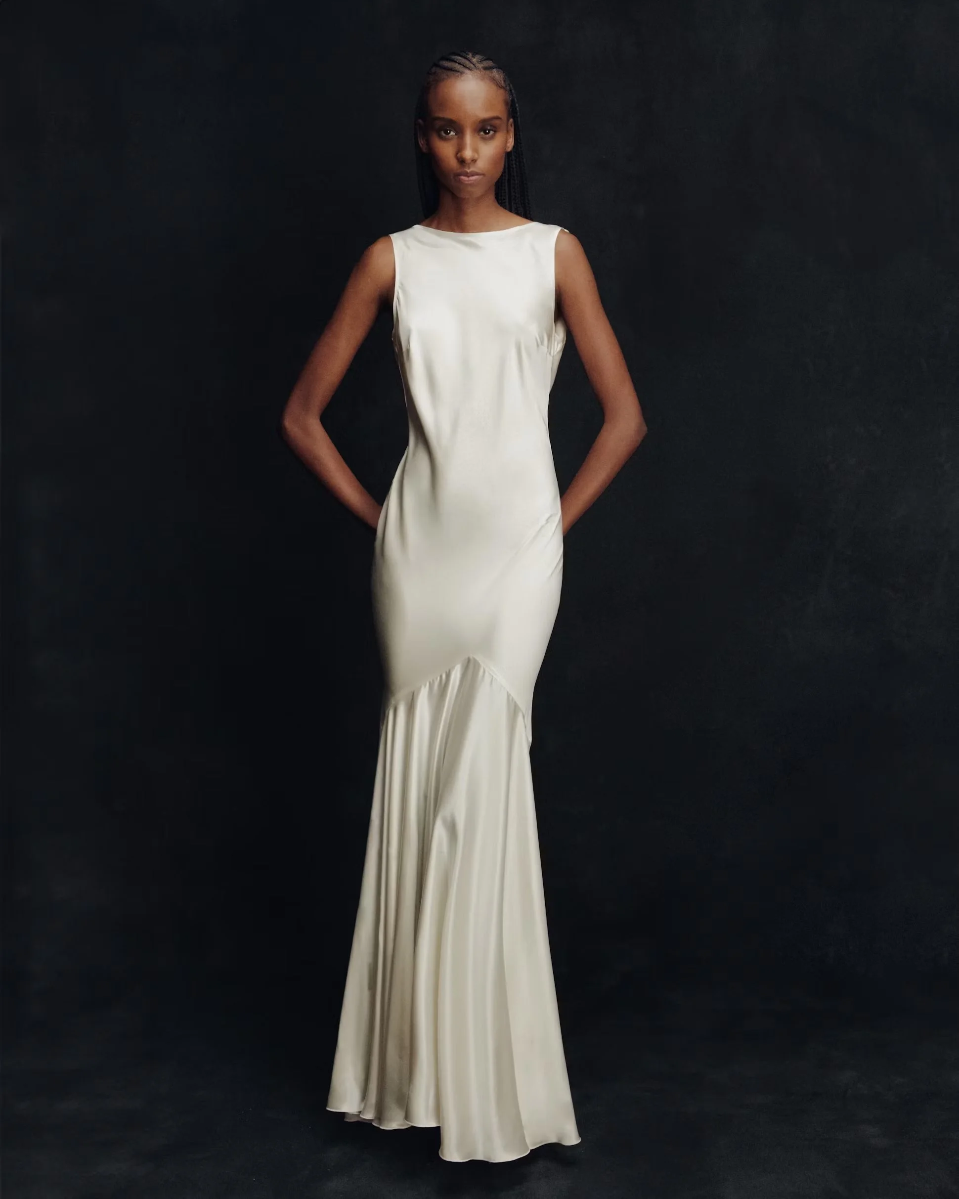 Model in an elegant ivory satin gown posing against a dark background, presenting timeless luxury and minimalist elegance.