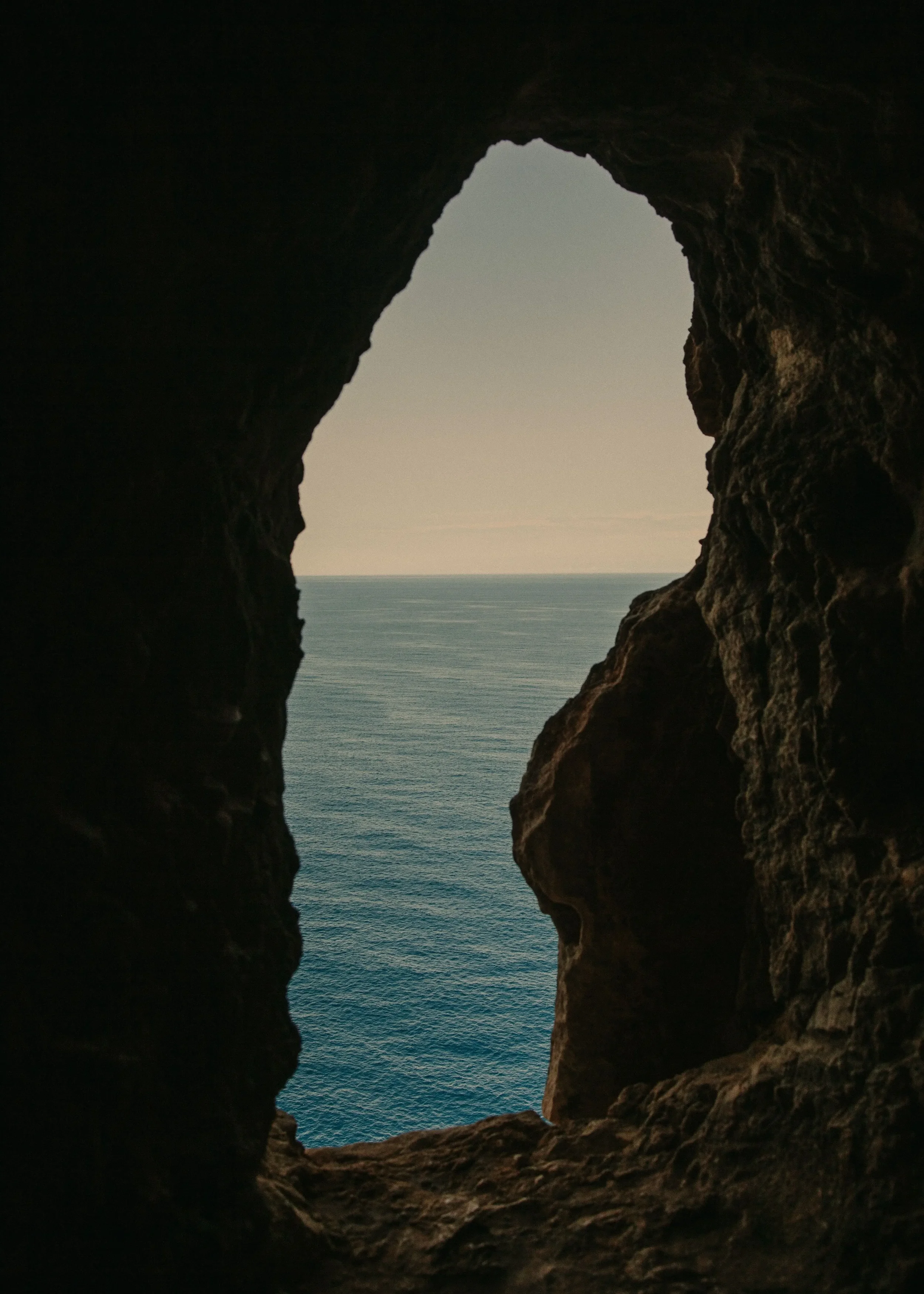 View of the tranquil Mediterranean Sea framed by the dark edges of a coastal cave, evoking serenity, depth, and a connection to nature’s raw beauty.
