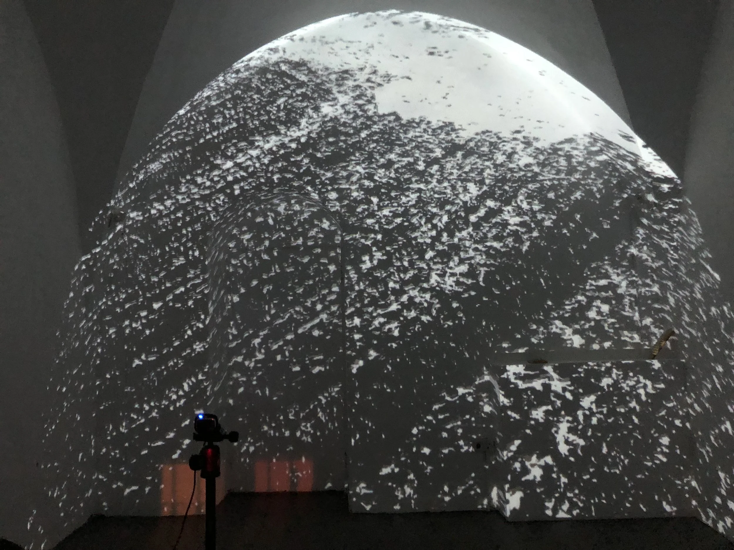 Black and white abstract projection of textured snow-covered terrain on a rounded wall with a stand and camera in the foreground.