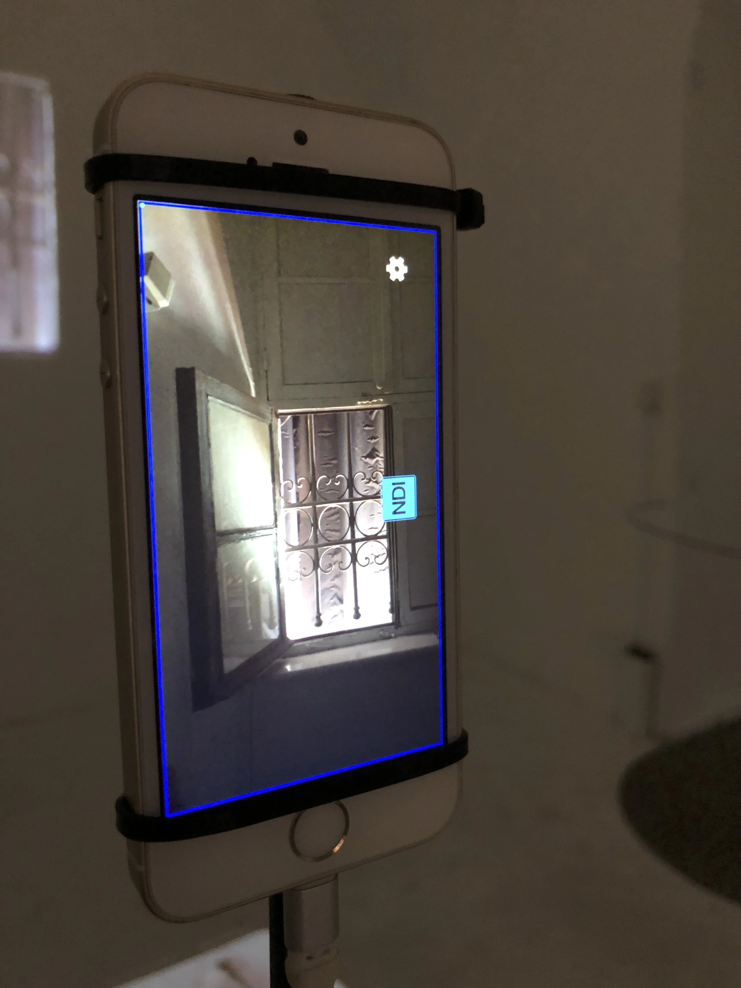Smartphone displaying an indoor scene with a window, a wrought iron security grille, and a label reading 'IND1'.