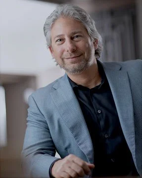 Andy Goldwasser, a male attorney at Ciano and Goldwasser, in Cleveland, Ohio with gray hair and a beard, wearing a light blue blazer over a dark shirt, sitting indoors.