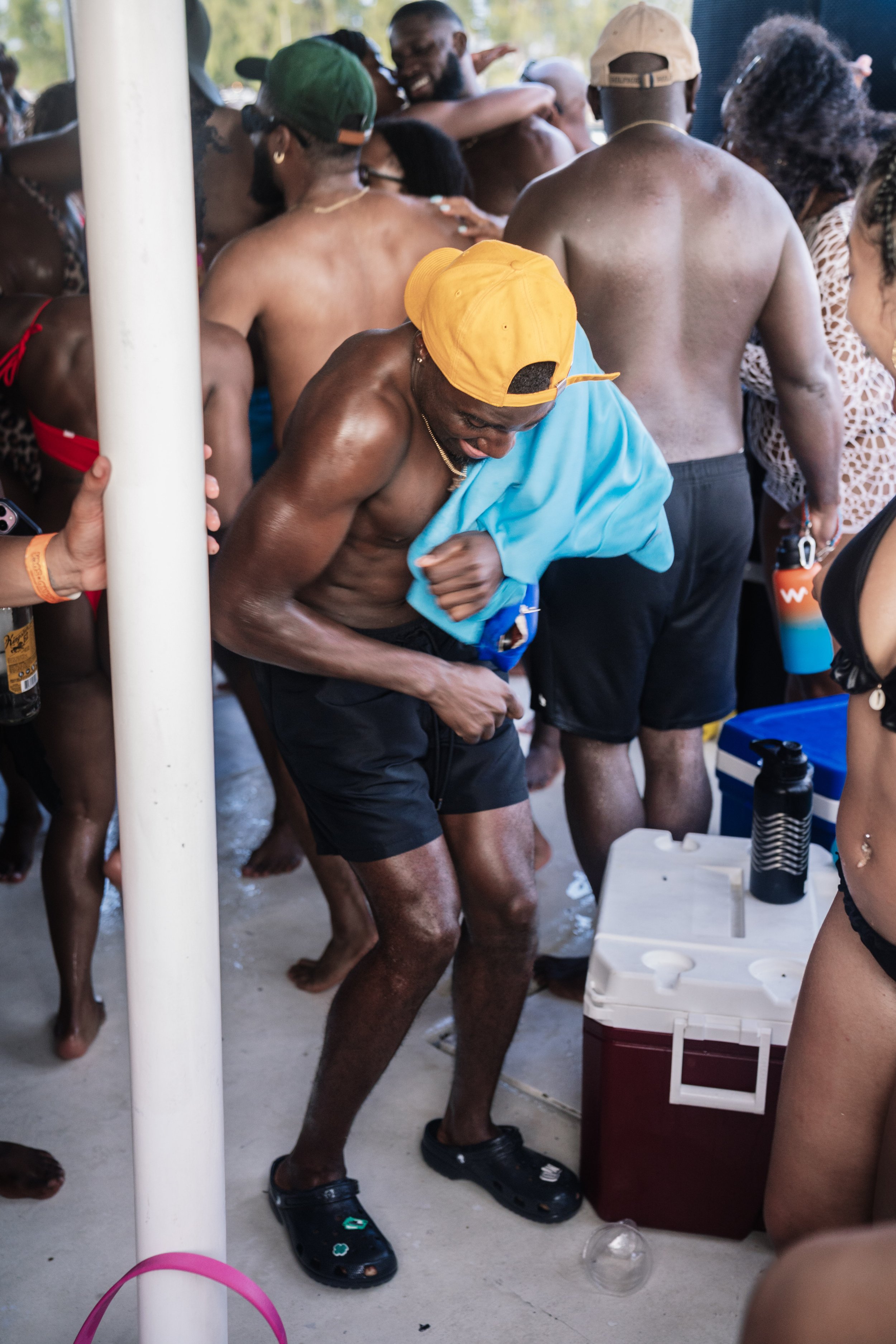 A group of people in swimsuits at a pool party, some dancing and enjoying drinks, with a cooler in the foreground.