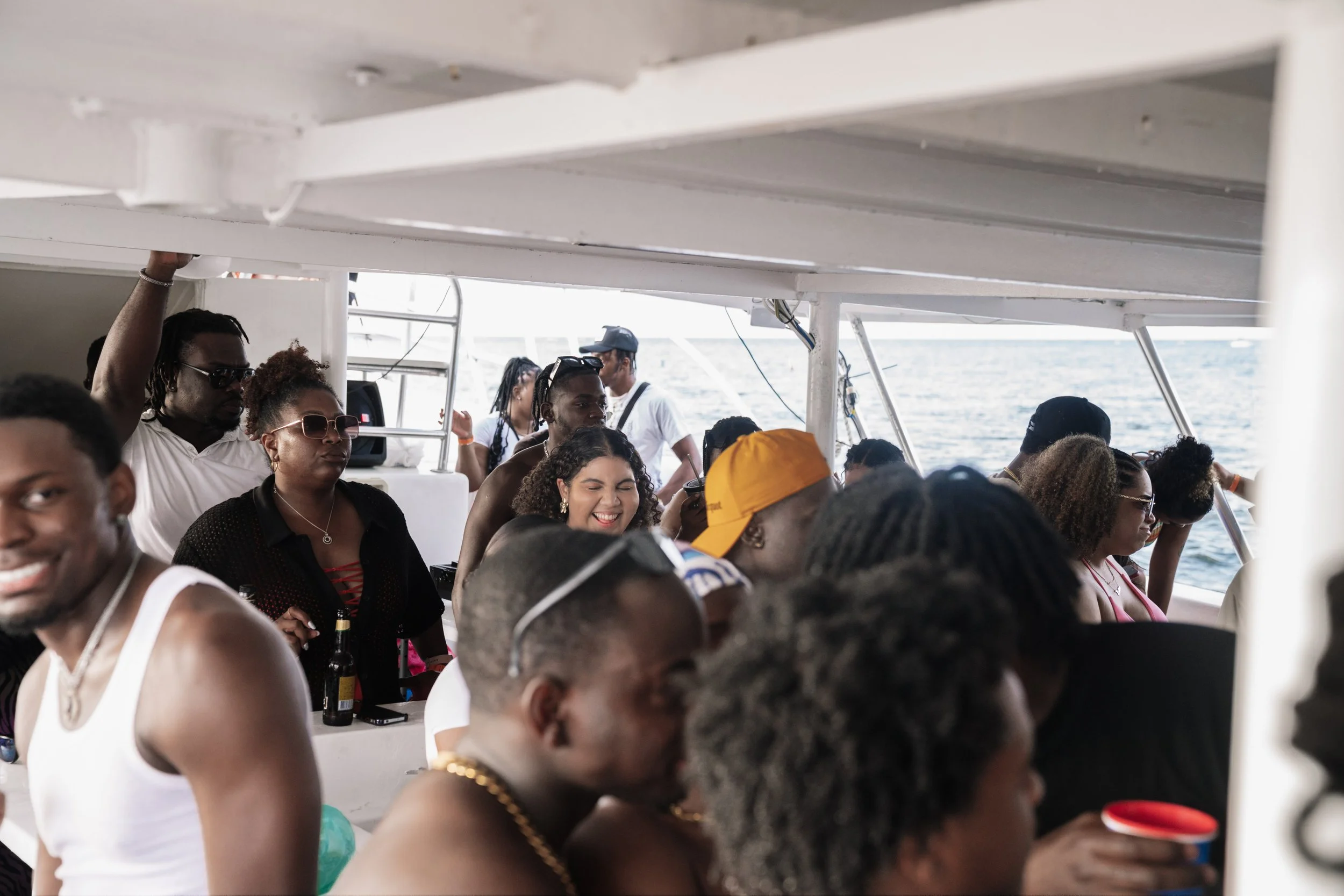 A diverse group of people enjoying a boat ride on the water, some smiling and some wearing sunglasses, with the ocean visible in the background.