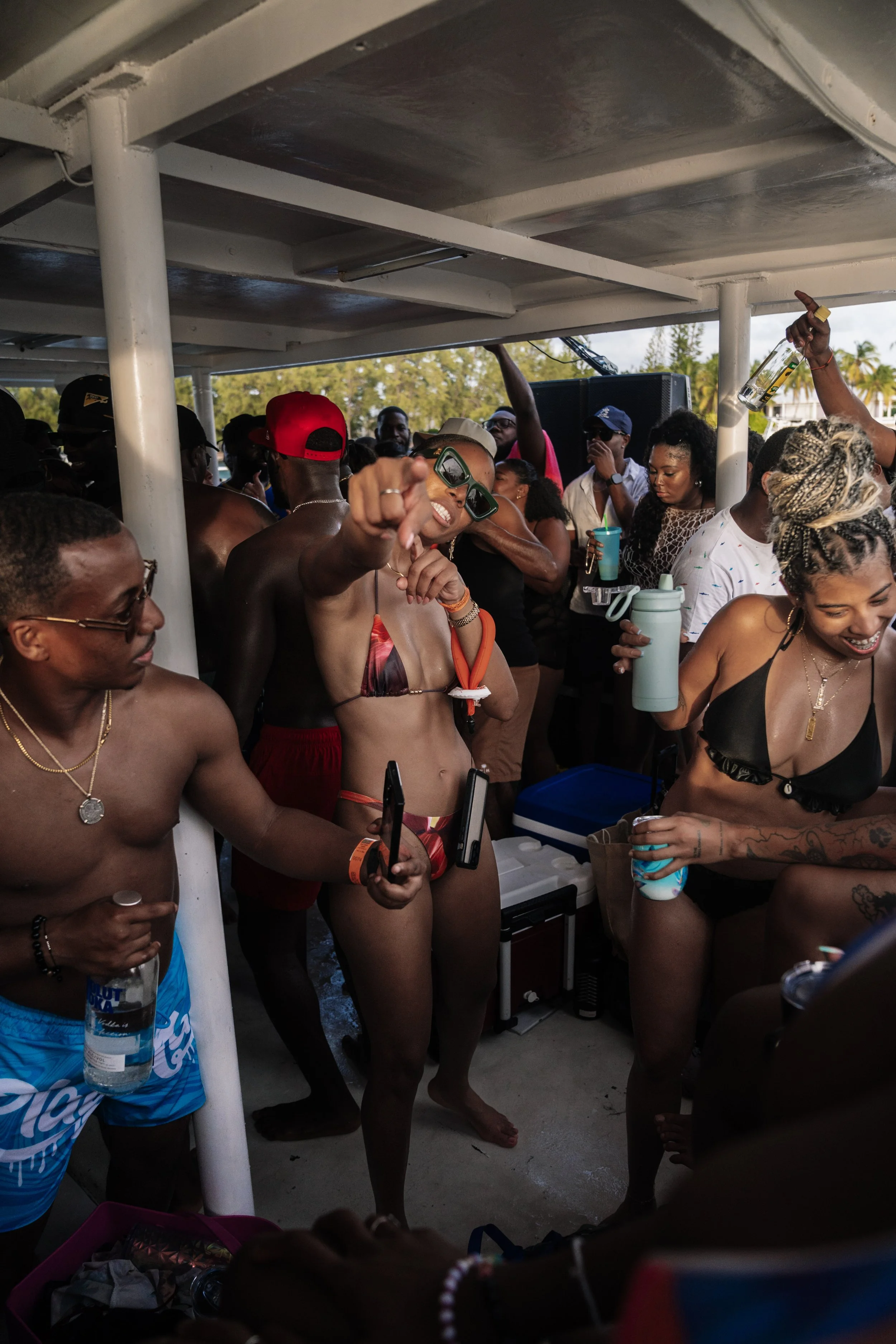 Group of people enjoying a pool party on a boat, with some dancing and holding drinks, wearing swimsuits.