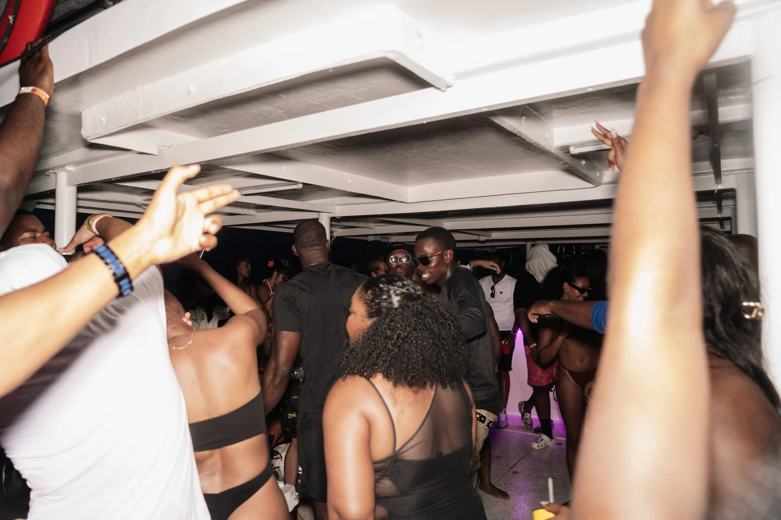 People dancing and socializing at a party, some wearing sunglasses and swimsuits, under a ceiling with white beams.