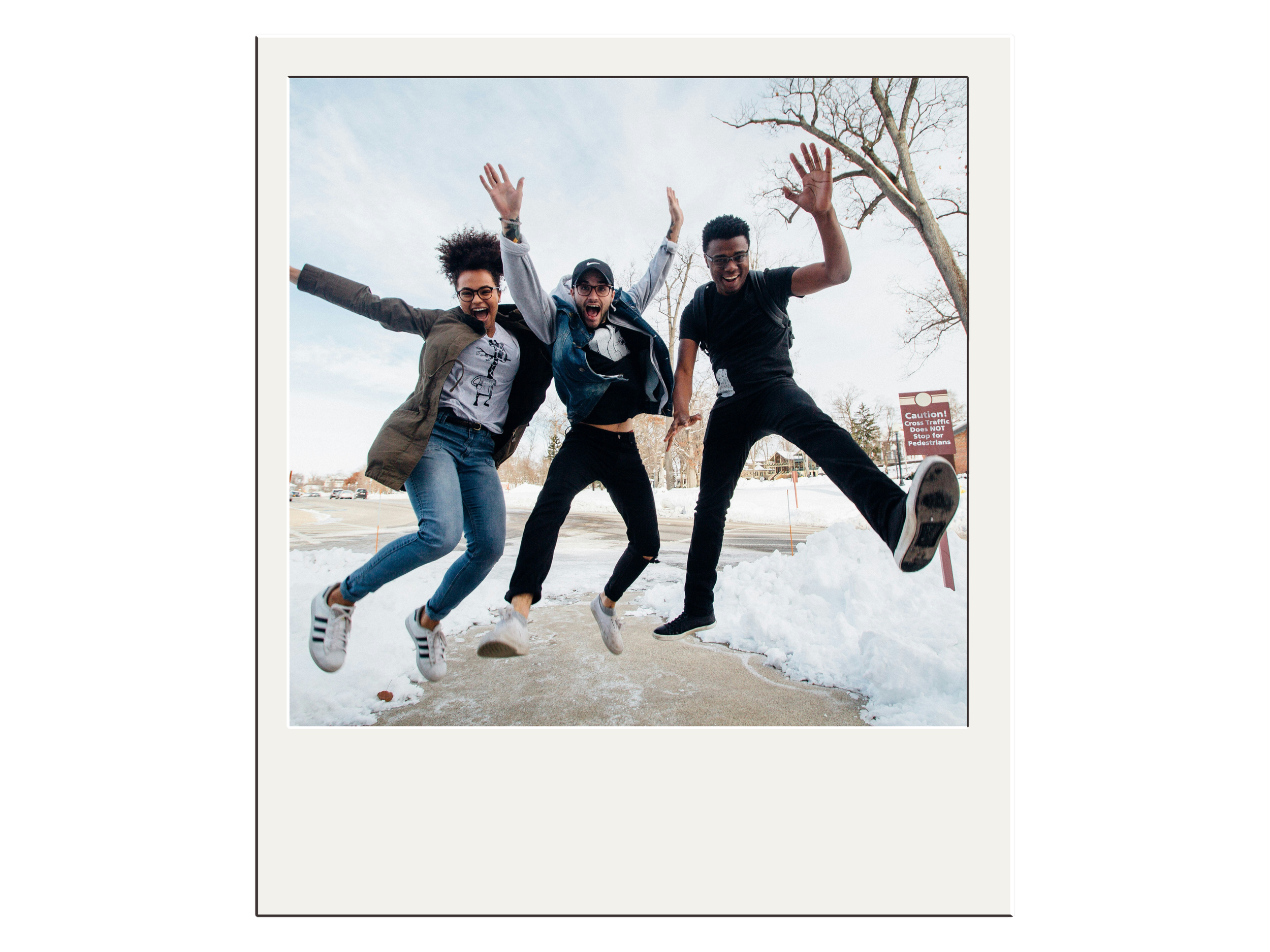 Three people jumping in the air on a snowy sidewalk, displaying excitement and joy against a winter backdrop.