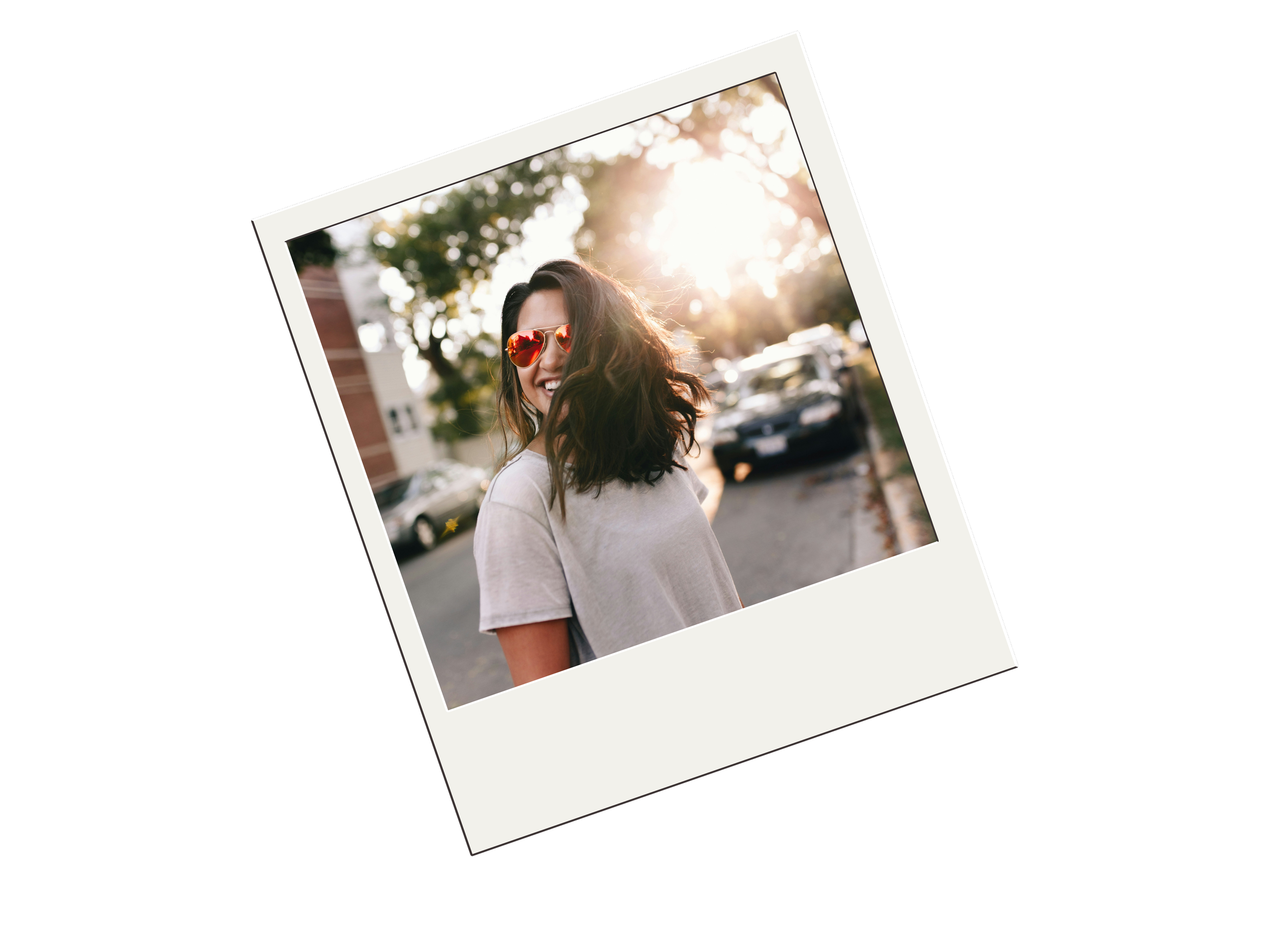 Woman in sunglasses smiling on a sunlit street, Polaroid style photo.