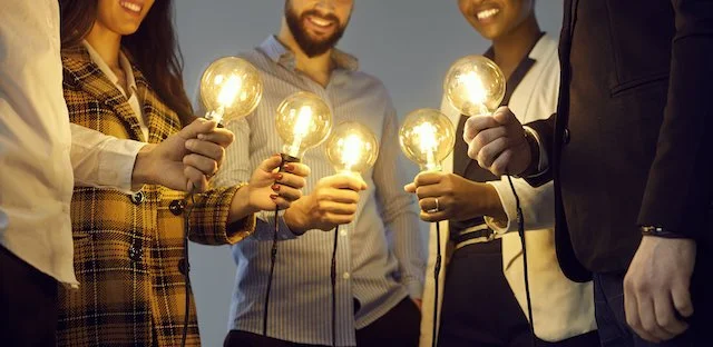 Group of people holding illuminated light bulbs, symbolizing collaboration and ideas.
