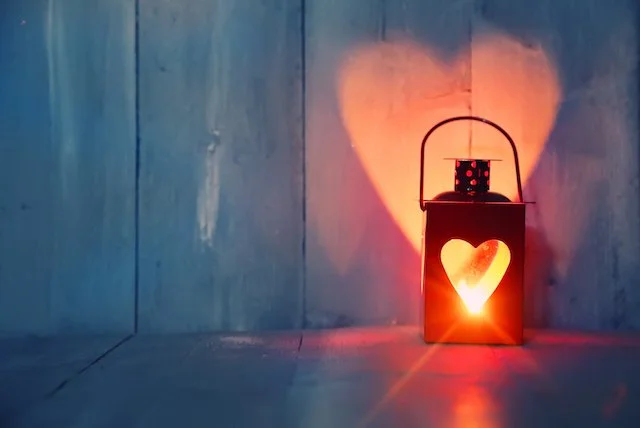 A red lantern with a heart-shaped cutout casting a warm glow on a wooden surface and wall.