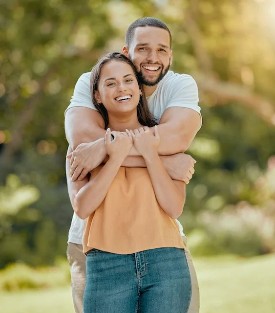A couple smiling and hugging outdoors.