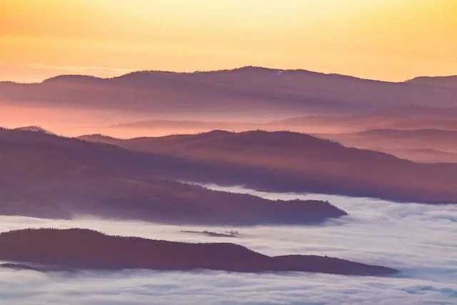 Sunrise over misty mountains with layers of fog and warm colors.