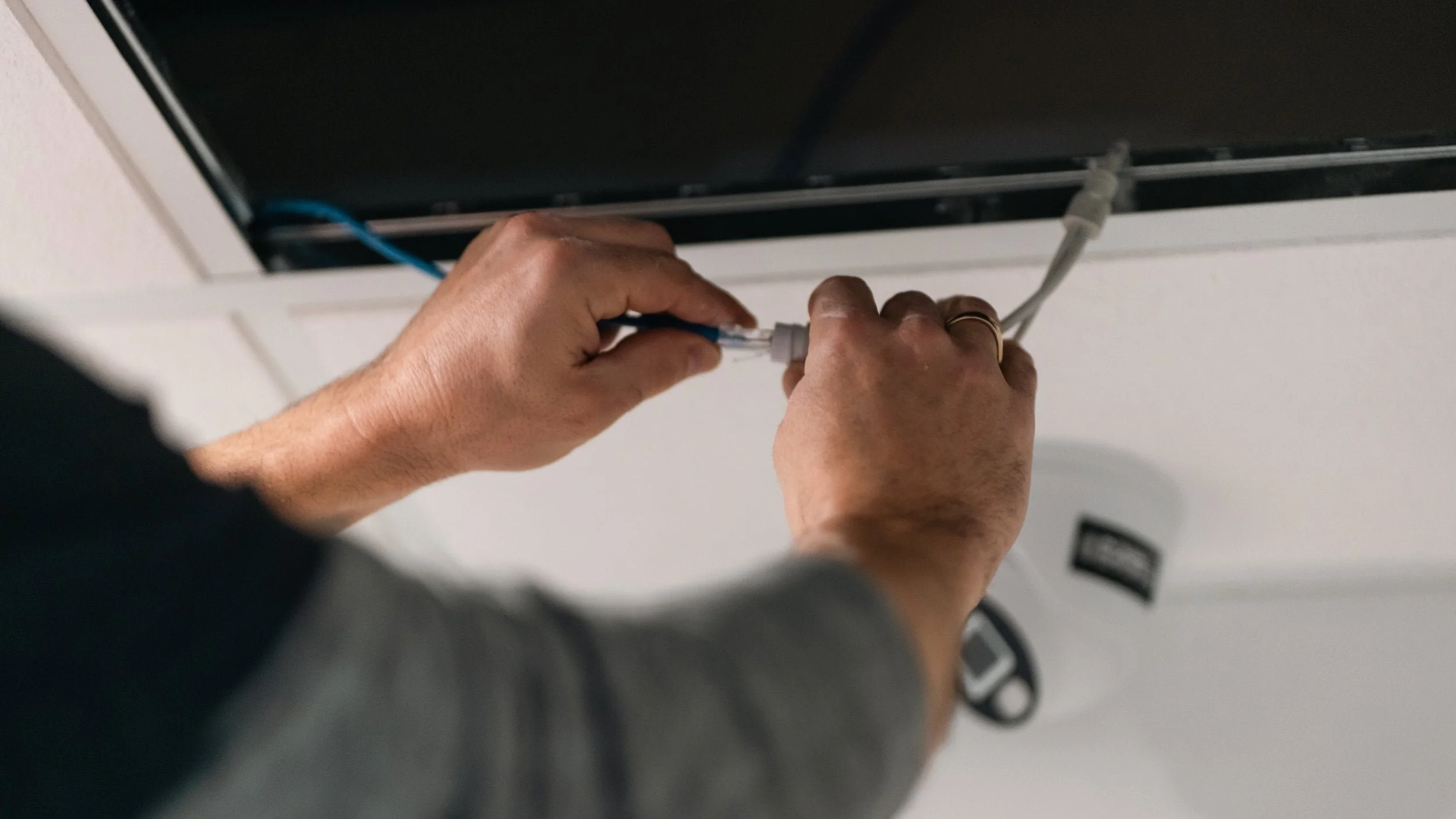 Hands connecting Ethernet cables to a device mounted on the wall.