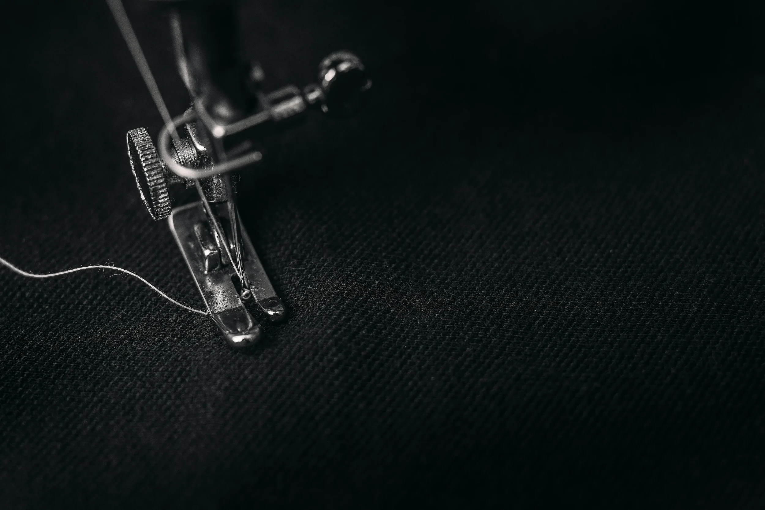 Close-up of a sewing machine needle sewing black fabric.