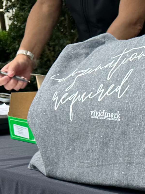 Person holding a pen near a bag with 'inspiration required' and 'vividmark marketing consultants' text.