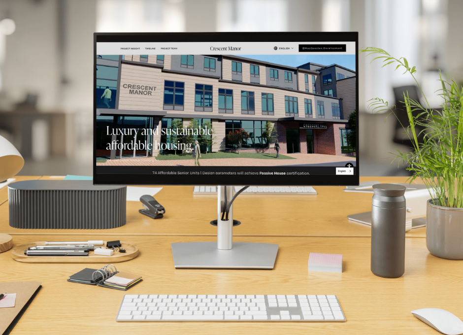 Office desk with computer monitor displaying Crescent Manor website featuring luxury sustainable housing.