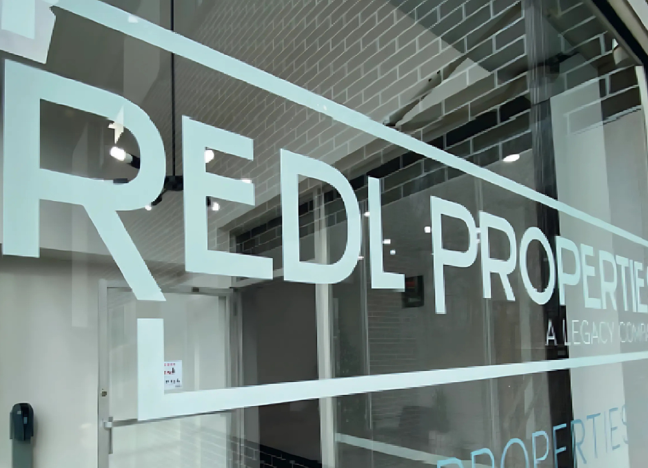 Glass storefront with "REDL PROPERTIES" logo and reflection of interior lighting.