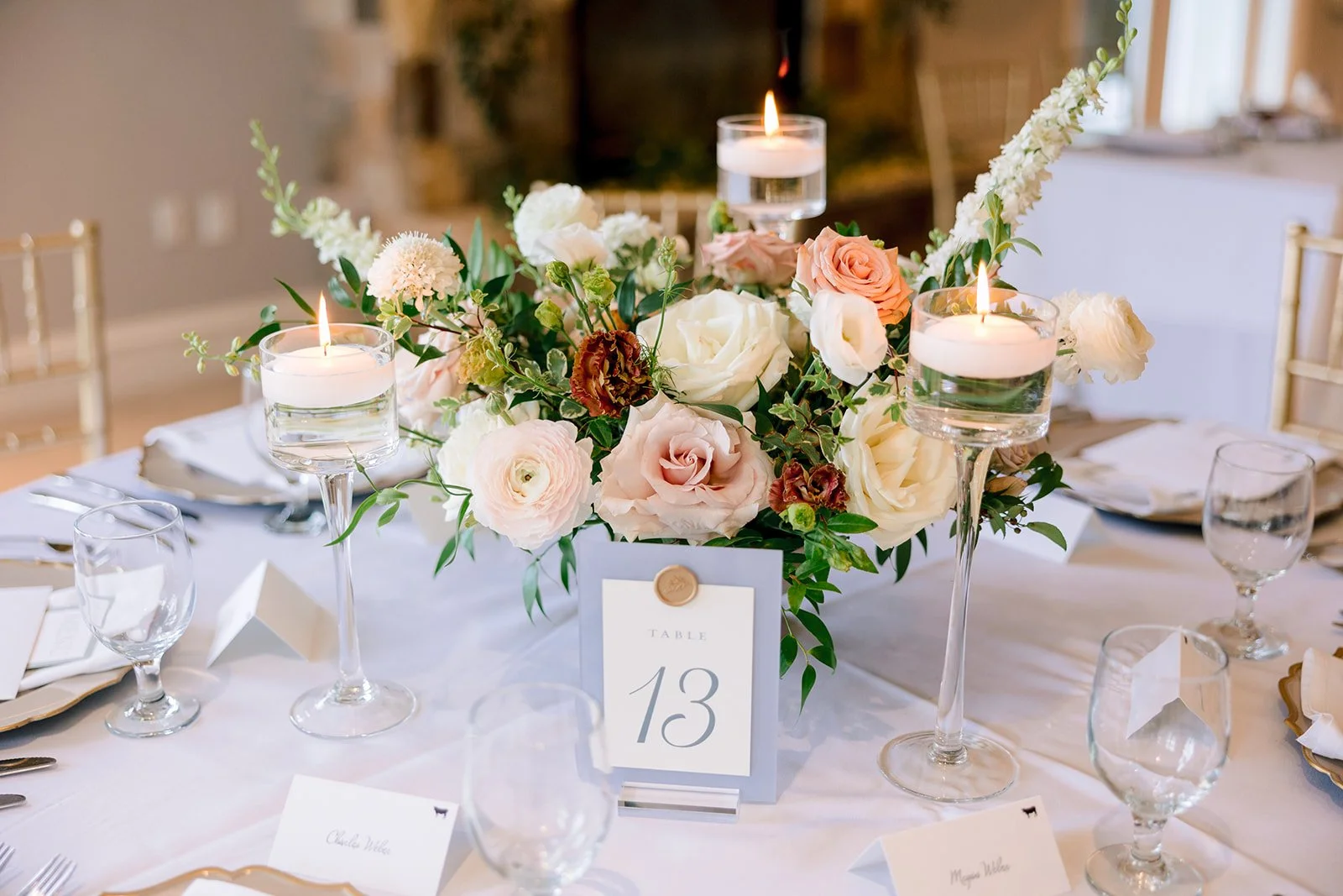 Elegant wedding table centerpiece with pink and white flowers and floating candles, table number 13 displayed on a card