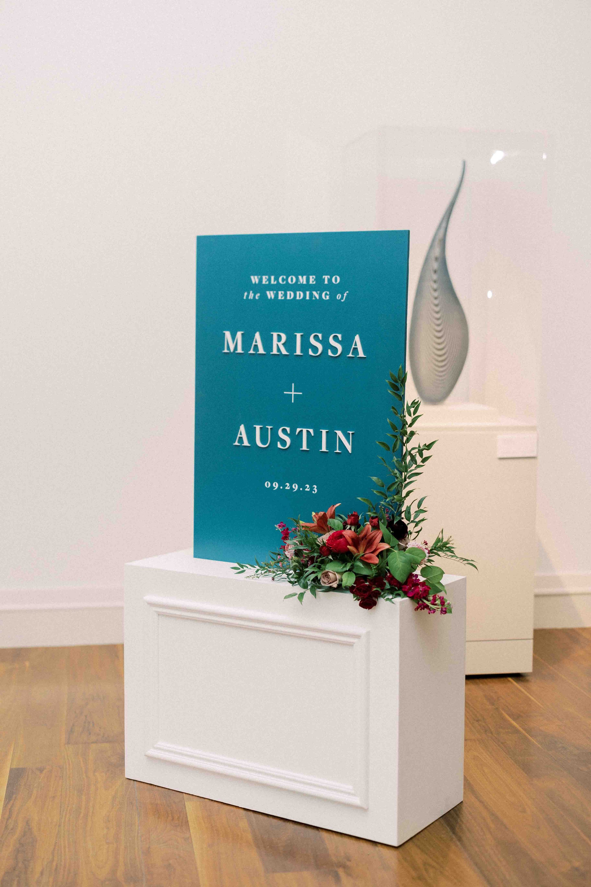 Wedding welcome sign with floral arrangements reading 'Welcome to the wedding of Marissa + Austin 09.29.23'.