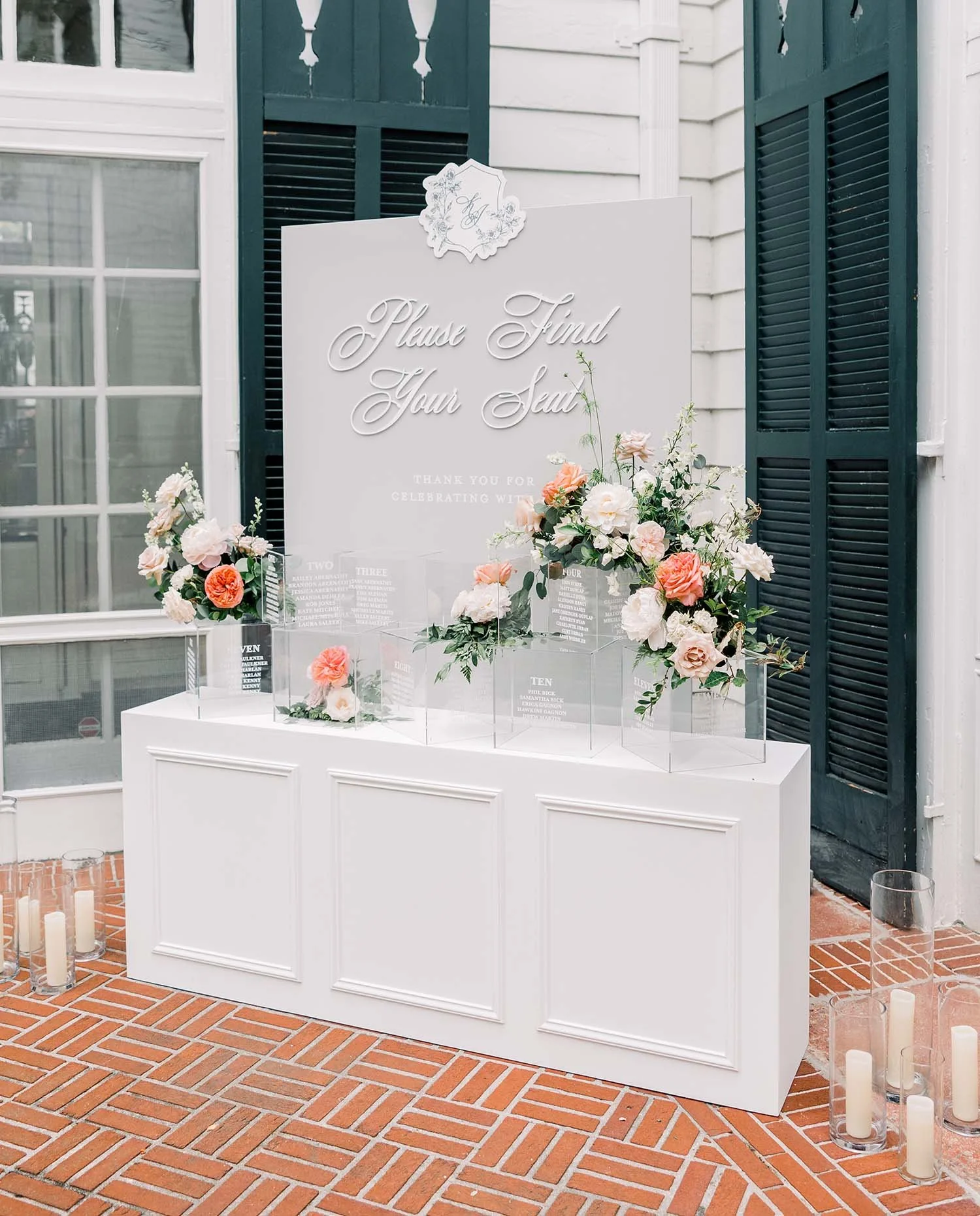 Wedding or event sign with floral arrangements and candles on brick floor.