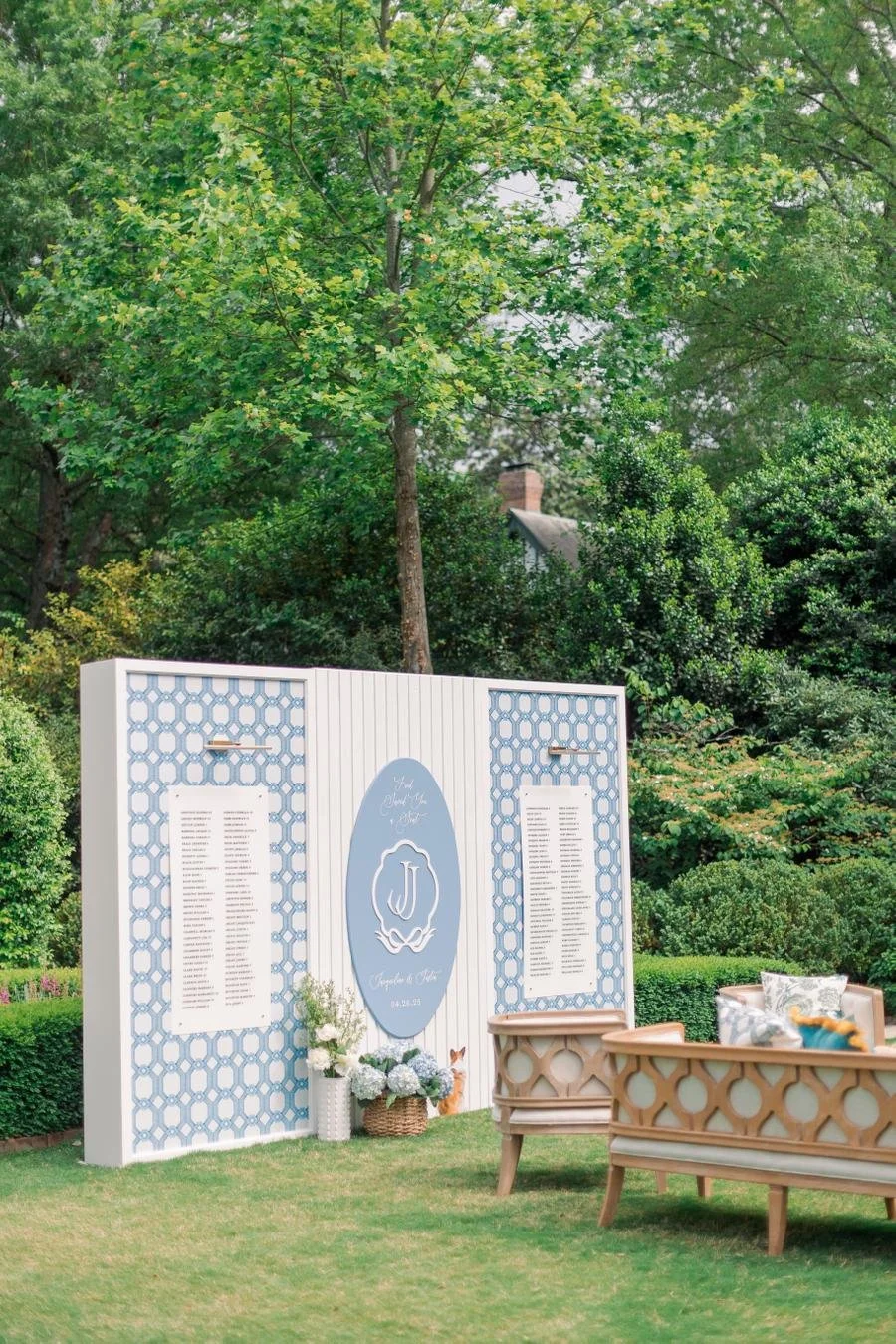 Outdoor wedding seating area with a decorative signboard displaying a seating chart, surrounded by lush green trees and bushes.