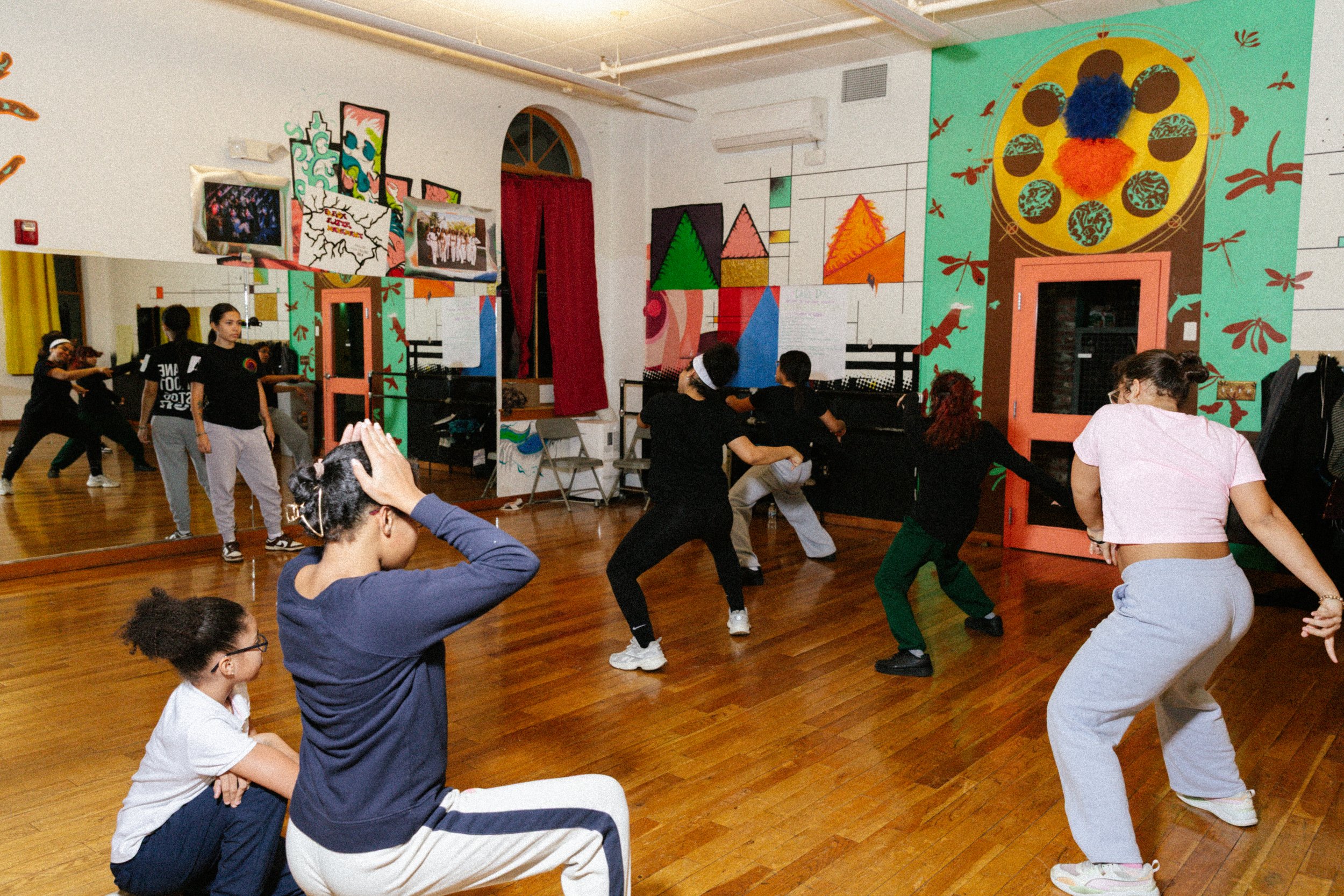 Group of people participating in a dance class or exercise session in a colorful studio with vibrant murals on the walls.