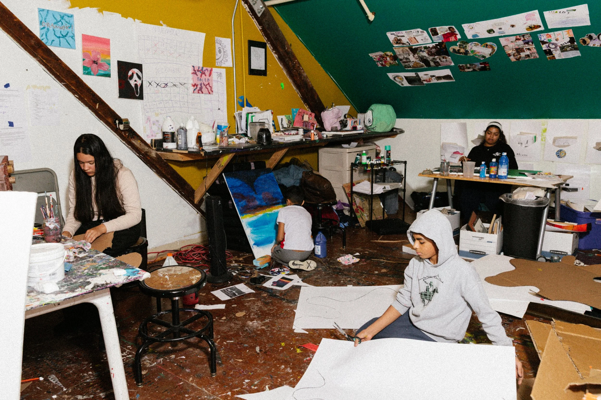 Children working on art projects in an art classroom with colorful paintings and supplies on the walls and tables.
