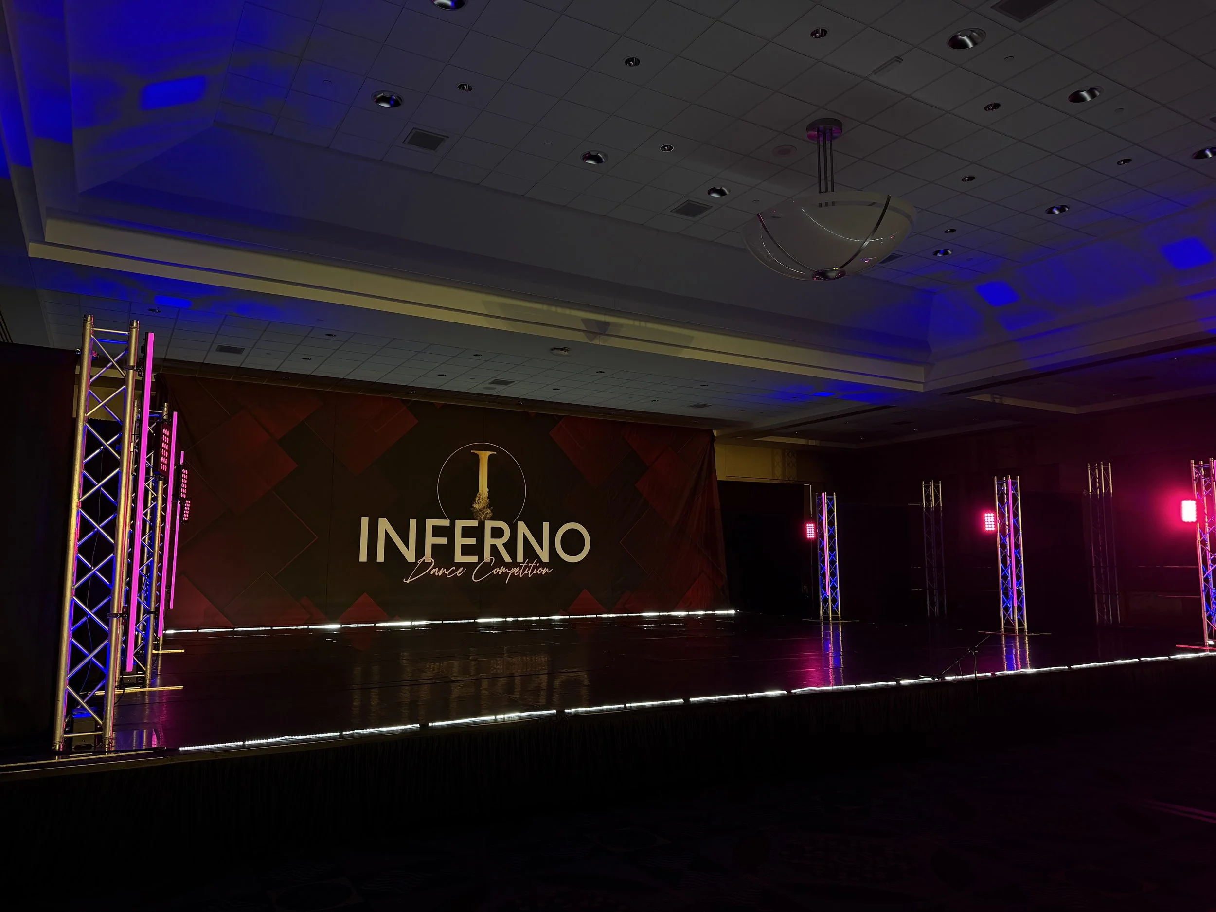 Empty stage with a backdrop displaying the words 'Inferno Dance Competition' and pink and purple stage lighting.