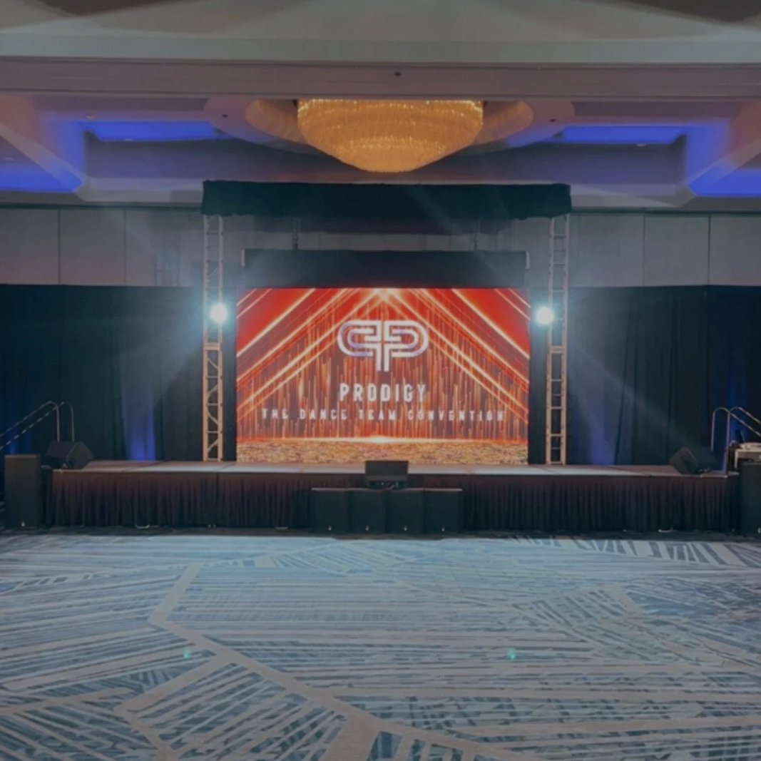 Empty stage with a large screen displaying the logo and text 'PRODIGY THE DANCE TEAM CONVENTION' at a dance event venue.