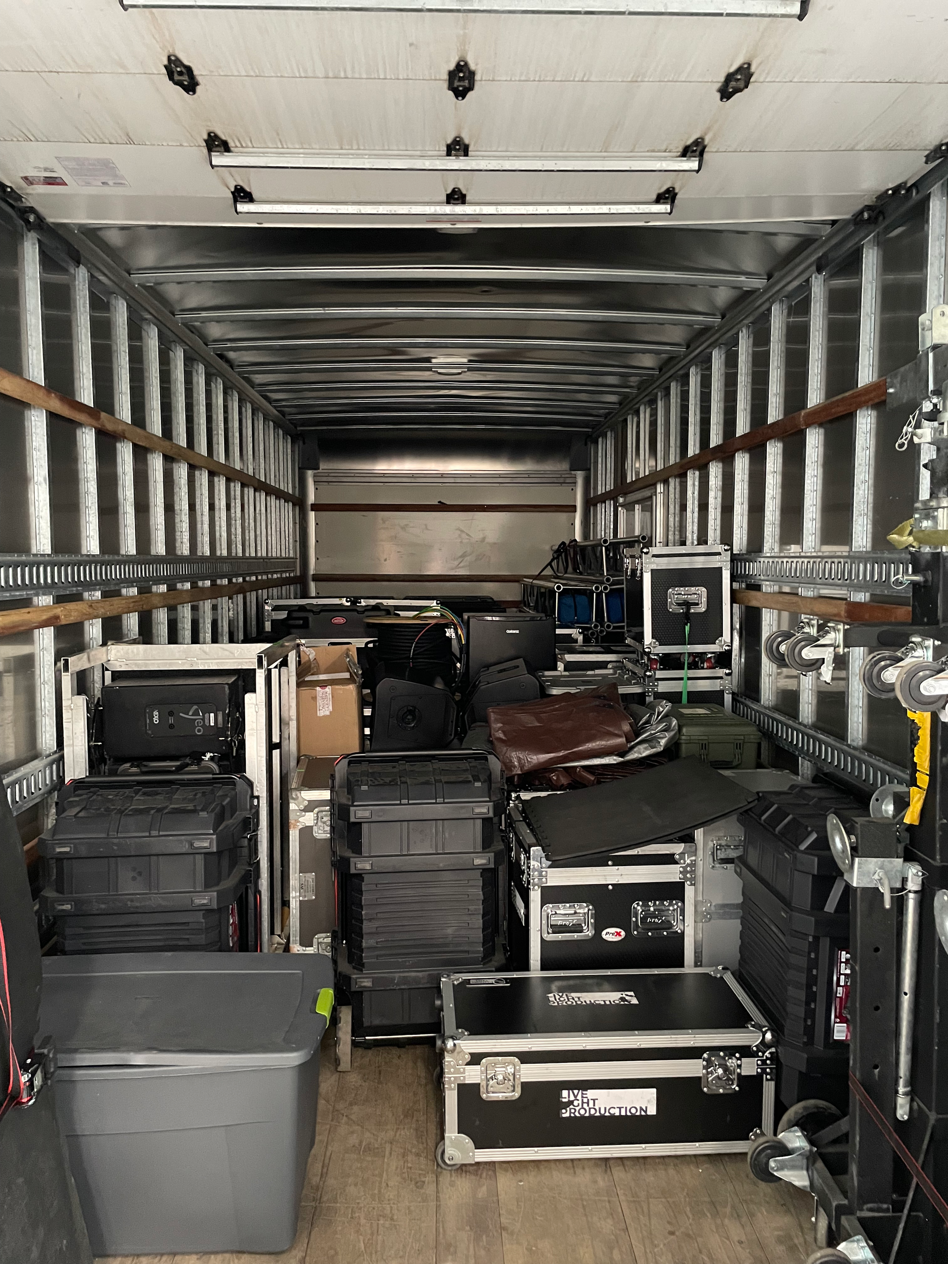 The back of an empty moving truck filled with black equipment cases, boxes, and equipment for a production or event setup.