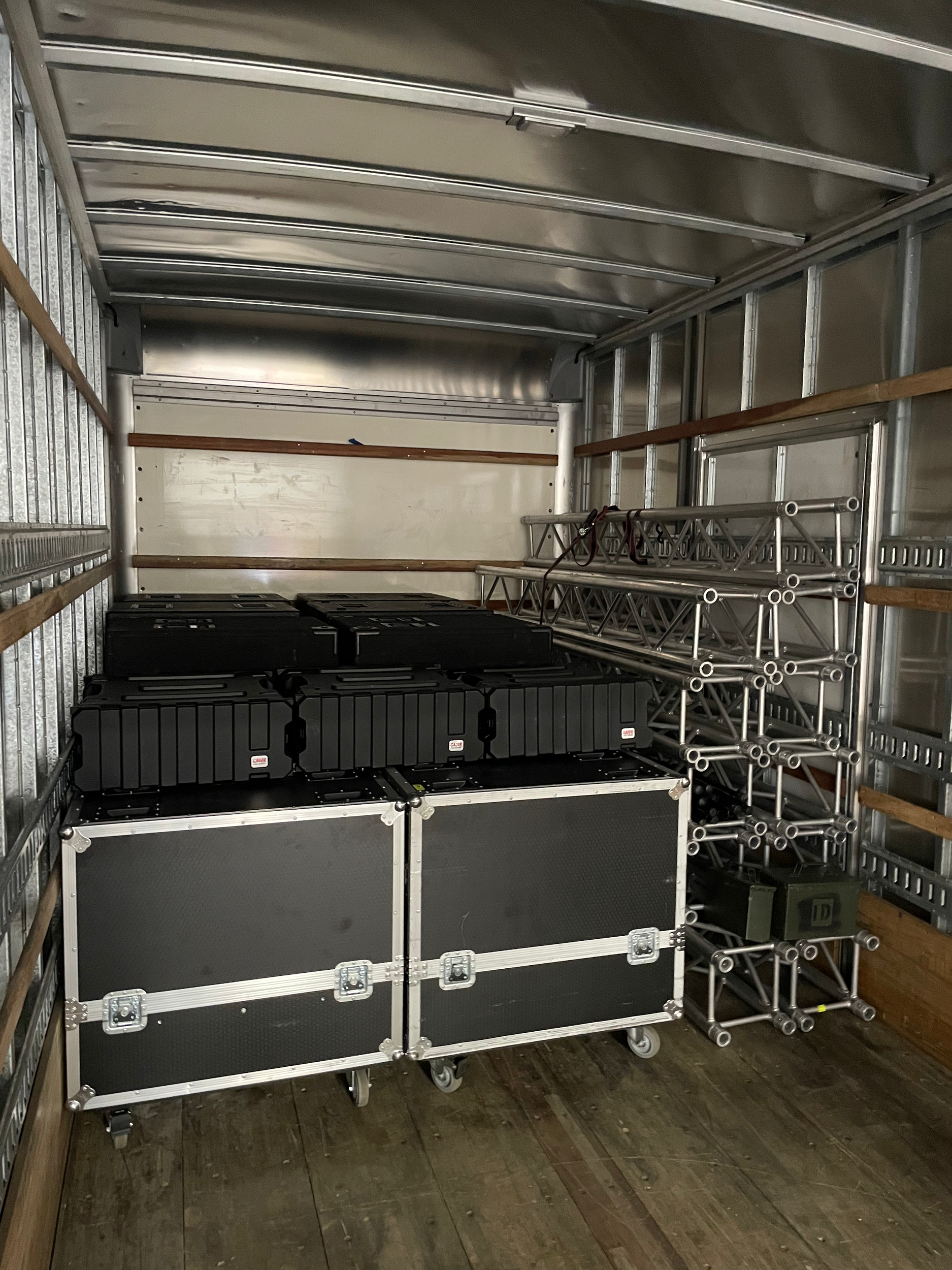 Empty metal storage unit containing black equipment cases, metal scaffolding, and wooden support bars, on a wooden floor.