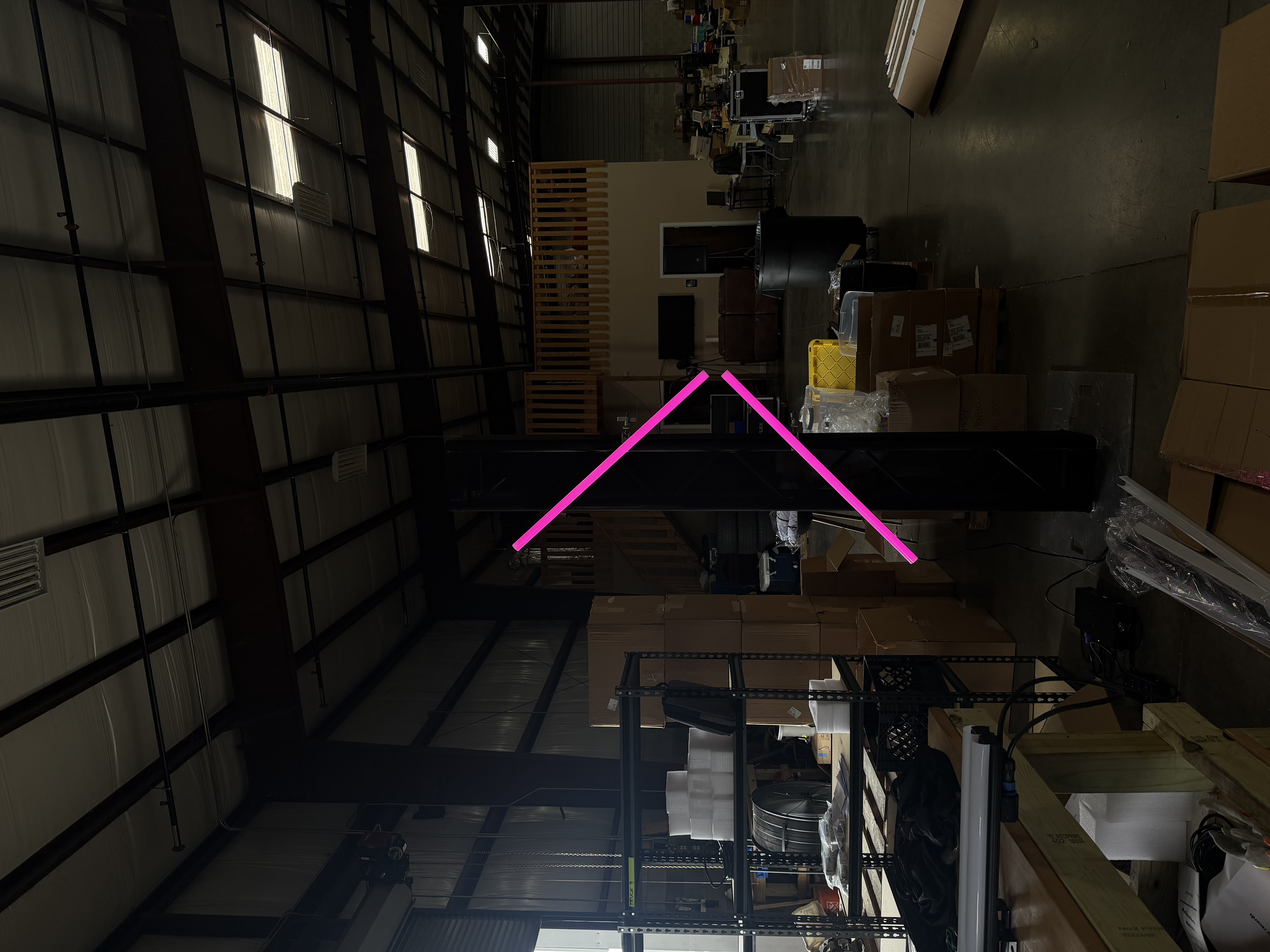 Interior view of a warehouse or storage space with shelves, boxes, and equipment, with natural light coming from skylights in the ceiling.