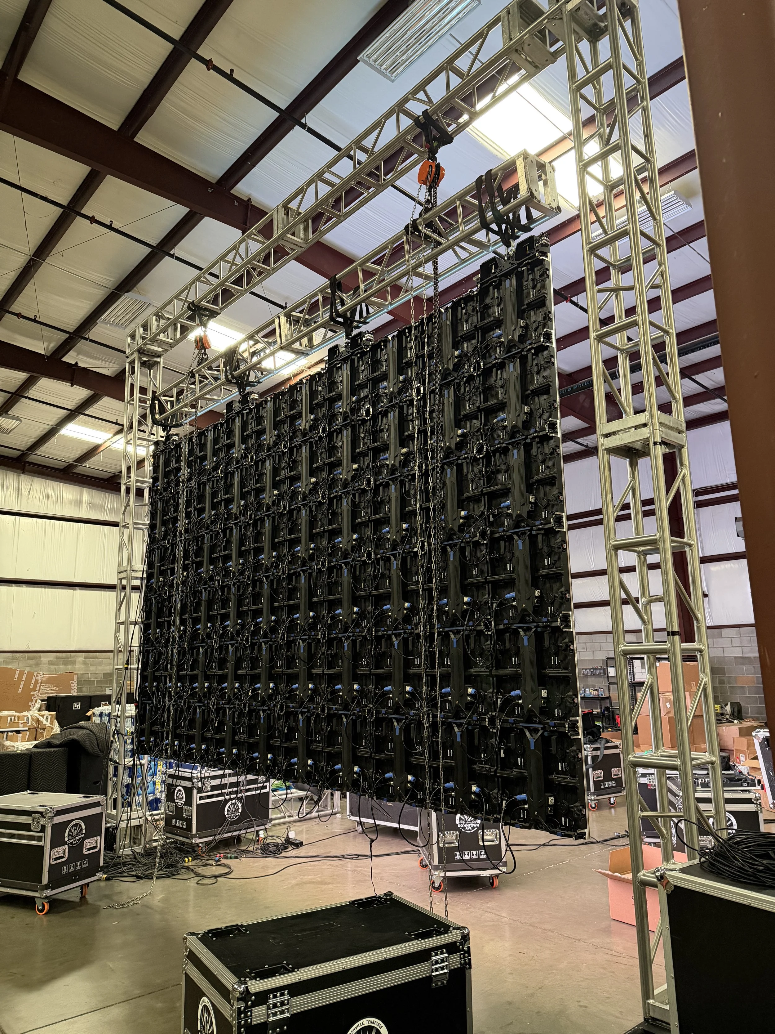 Stage setup with multiple electronic screens and lighting trusses in a warehouse or industrial space.