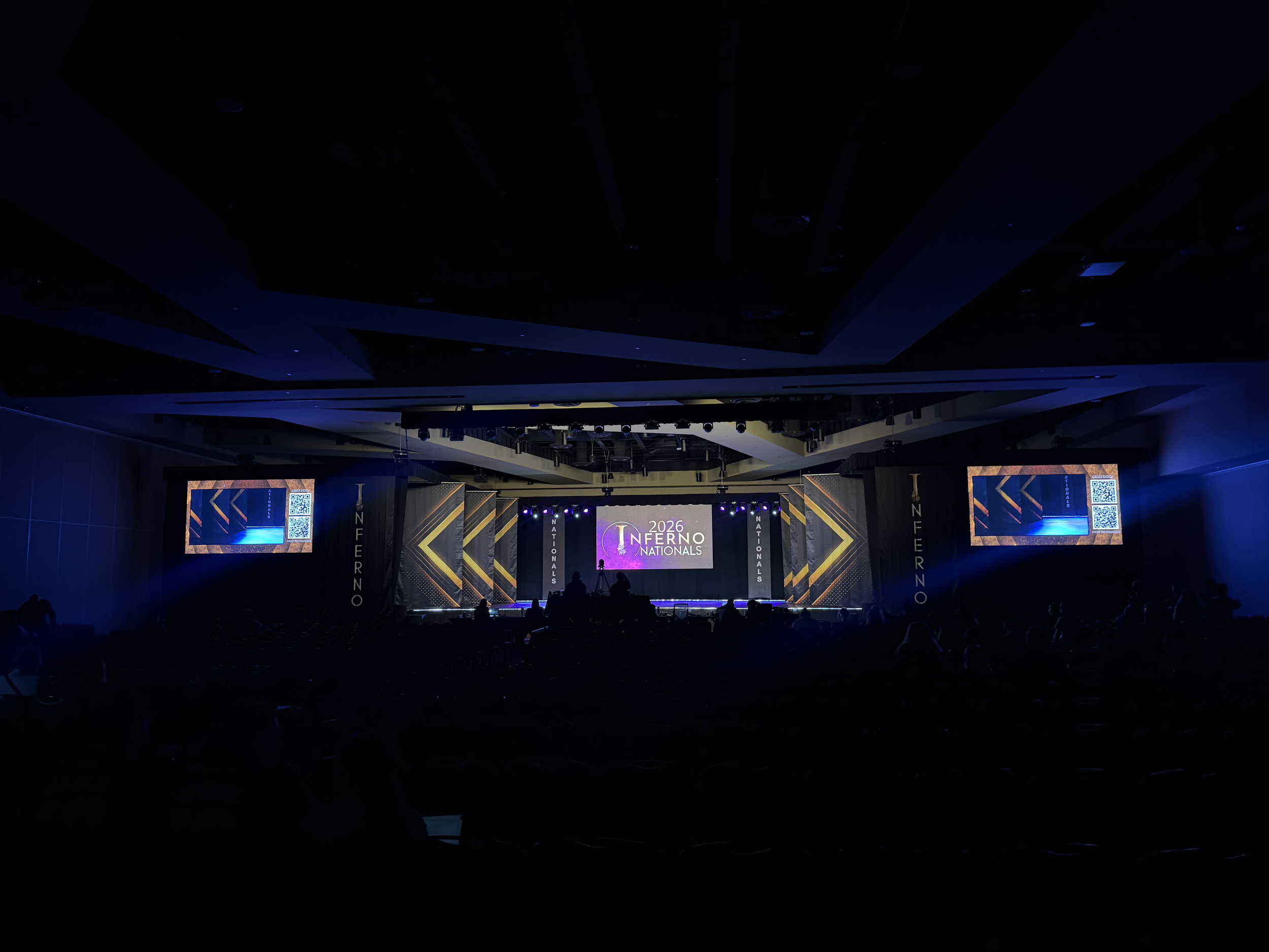 Stage with screens displaying the text '2026 Inferno Nationals' and a few people in the audience, inside a large indoor venue.